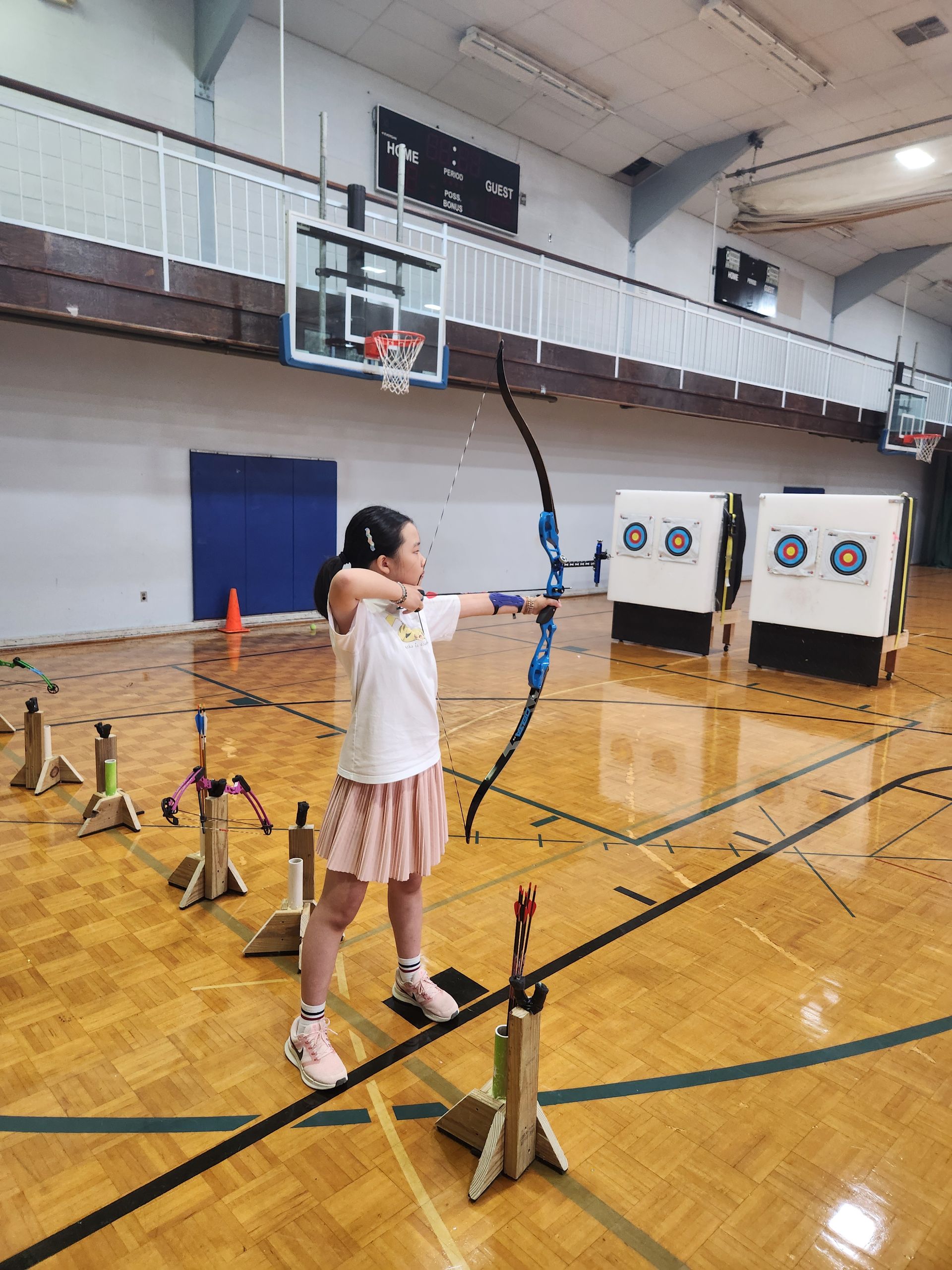 Person aiming a bow at targets in a gymnasium during archery practice