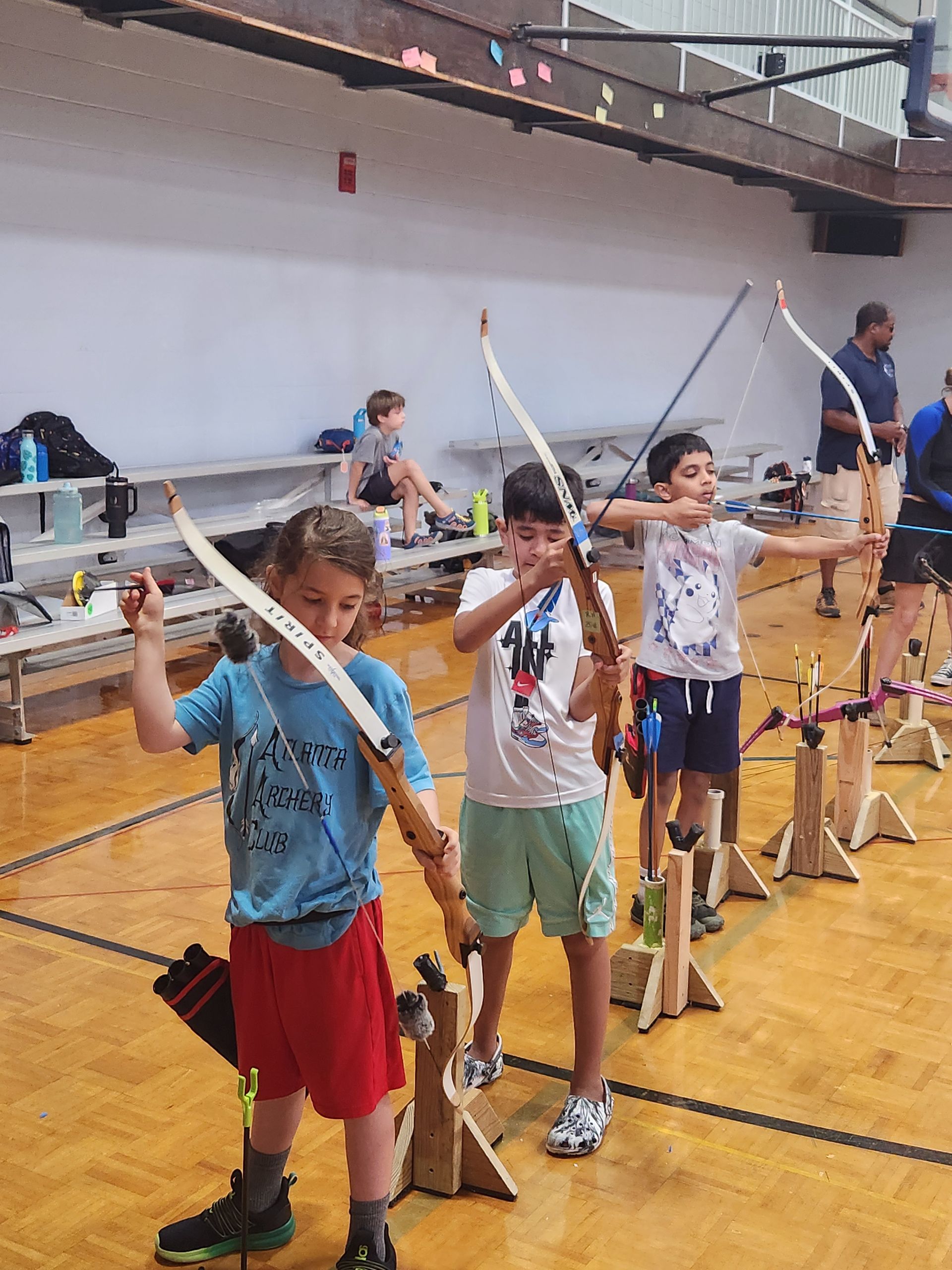 Children holding bows and arrows in a gym during an archery activity