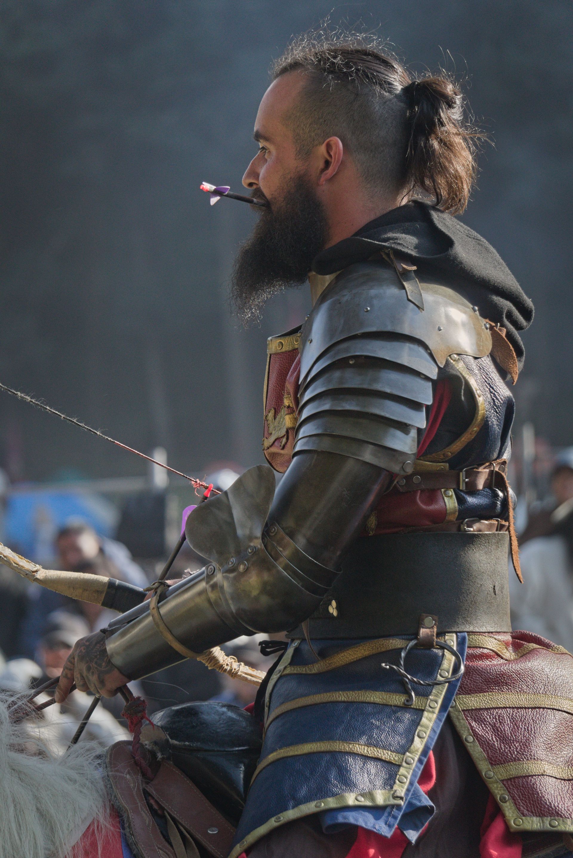 Person aiming a bow and arrow outdoors, with a blue-fletched arrow drawn back.