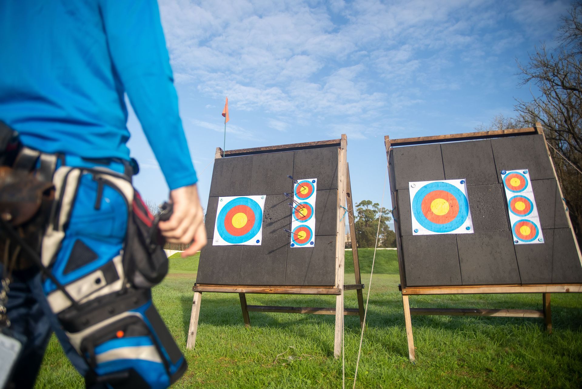 Archer in blue stands before two targets on a grassy archery range.