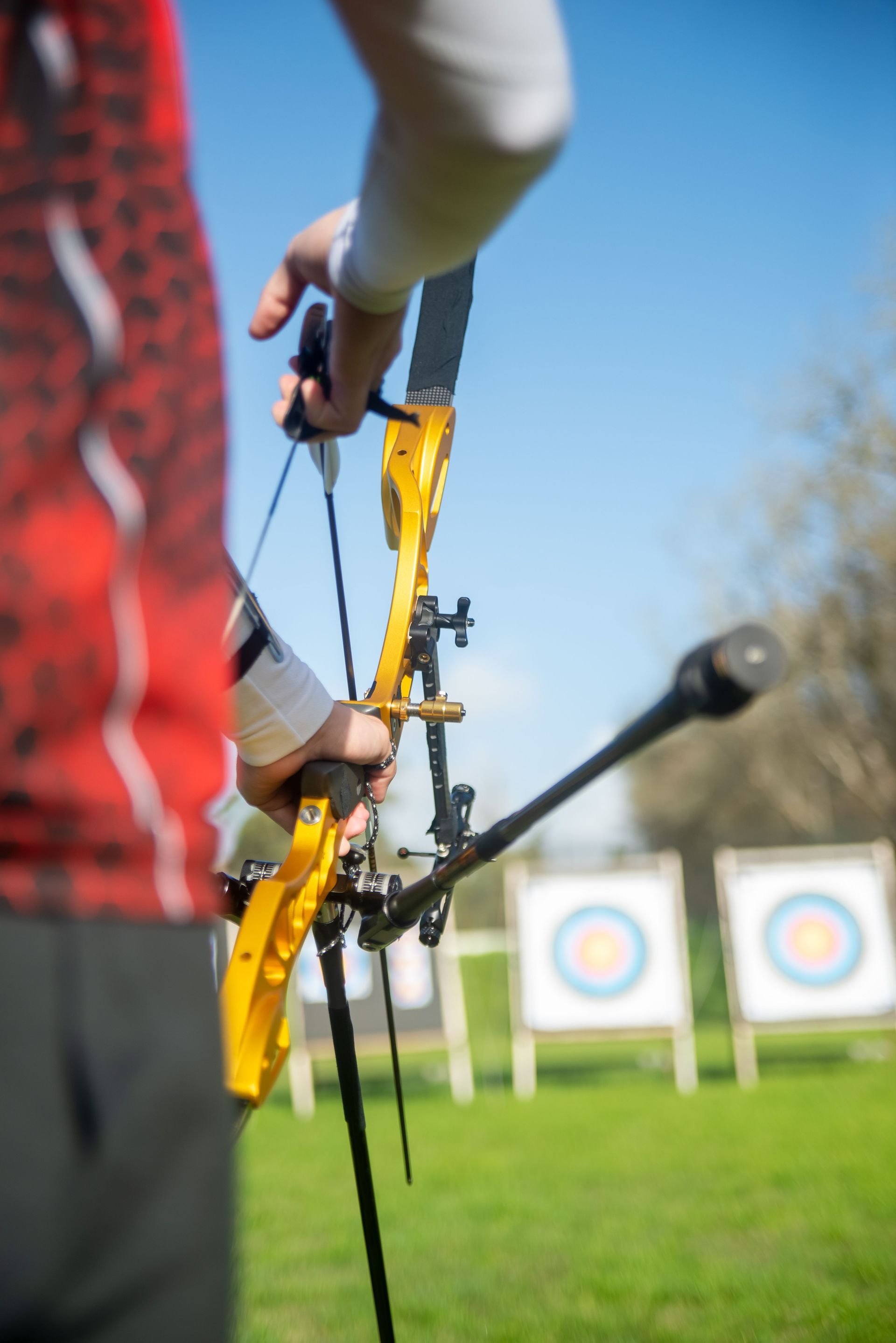 Archery target practice with a yellow bow and arrow aimed at distant targets on a grassy field.
