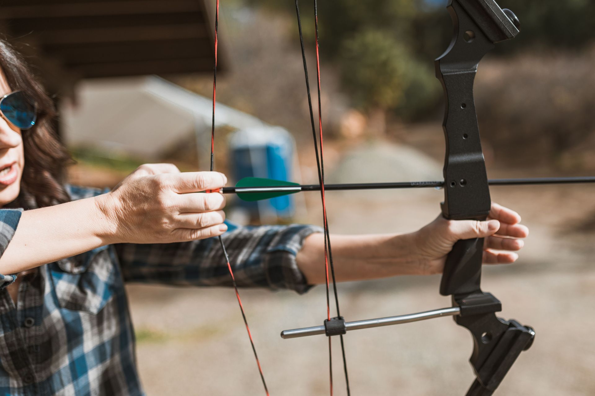 Person aiming a bow and arrow outdoors, with a blue-fletched arrow drawn back.