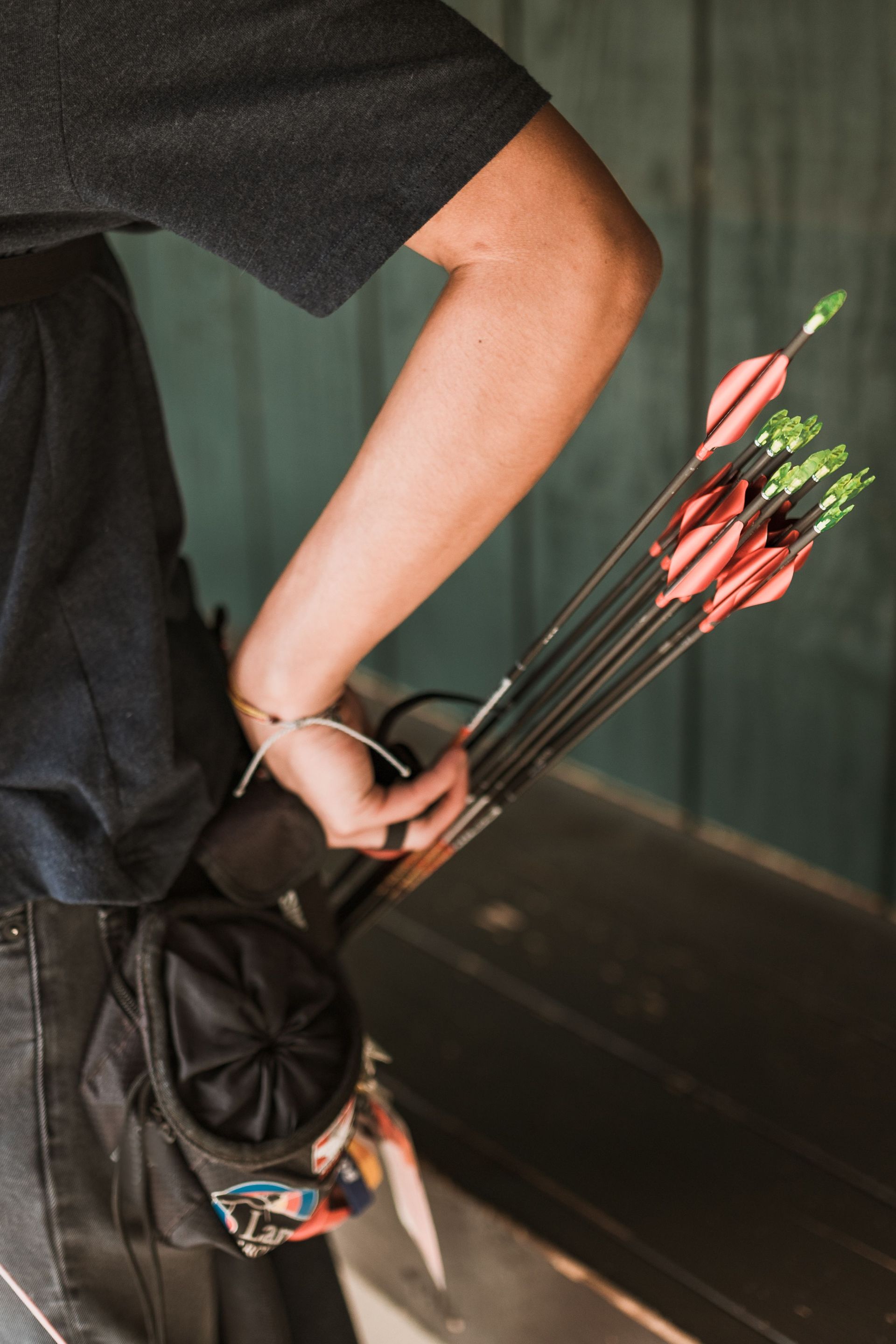 Person holding a bouquet of red arrows in a quiver, wearing a black shirt against a dark wall.
