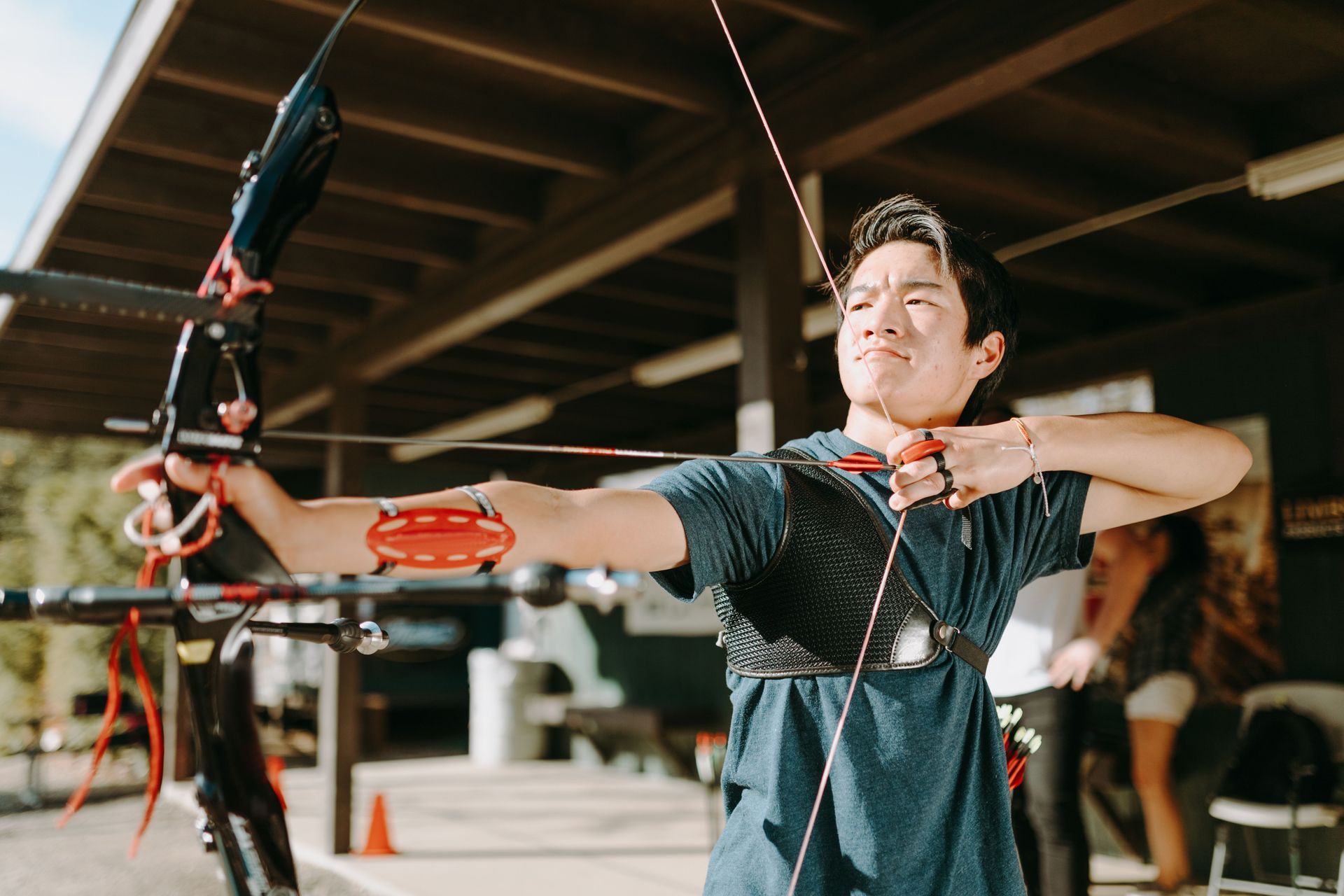Person aiming a red compound bow indoors, with focused expression.