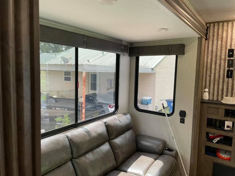 Cozy RV living area with gray couch, large windows, and beige curtains overlooking a neighborhood