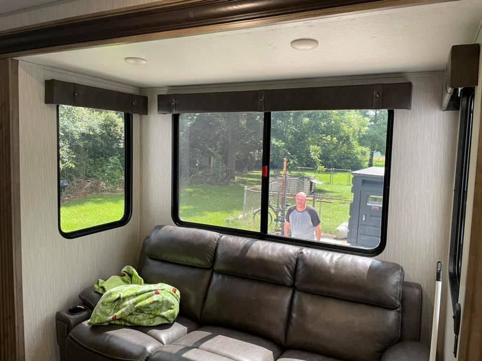 RV interior with brown sofa, green blanket, and person visible outside through the window