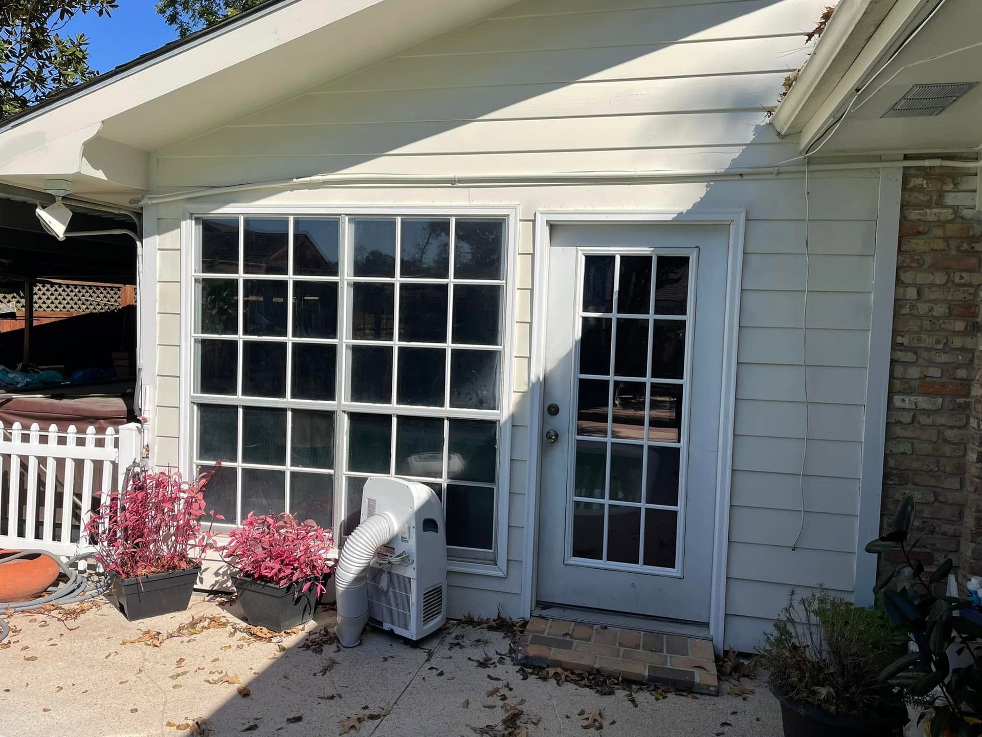 White-sided house exterior with large window, glass door, and an air conditioner unit outside