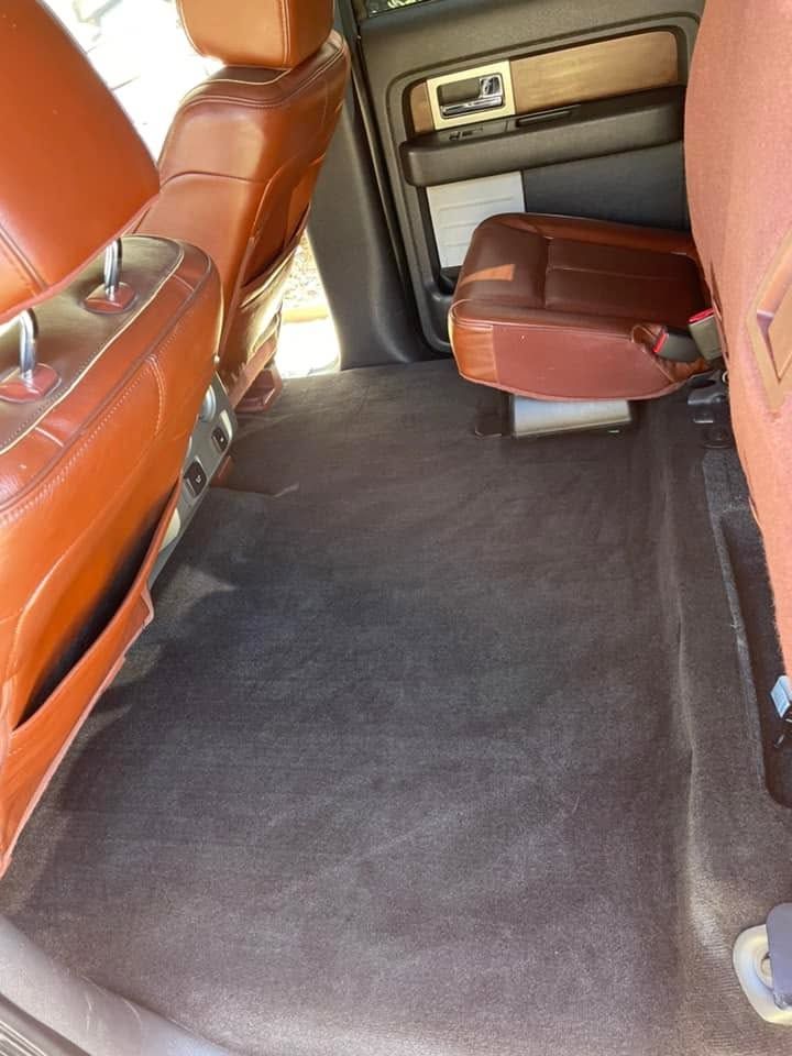 Car interior with brown leather seats and a dark carpeted floor, viewed from the rear seat area