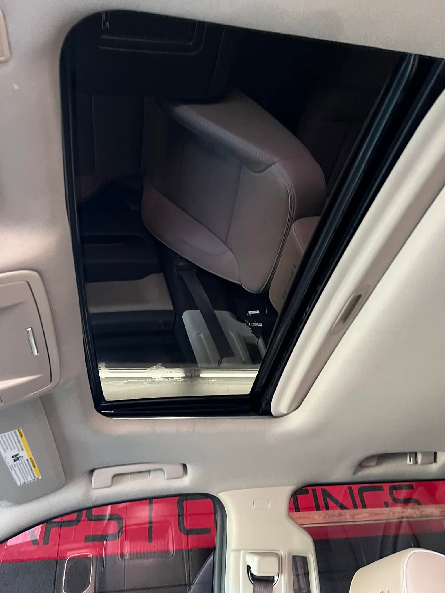 Interior of a car with a sunroof open, showing the roof lining and back seat area.