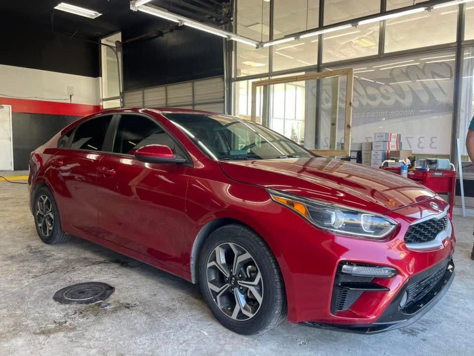 Red sedan parked inside a garage with a concrete floor and open bay doors