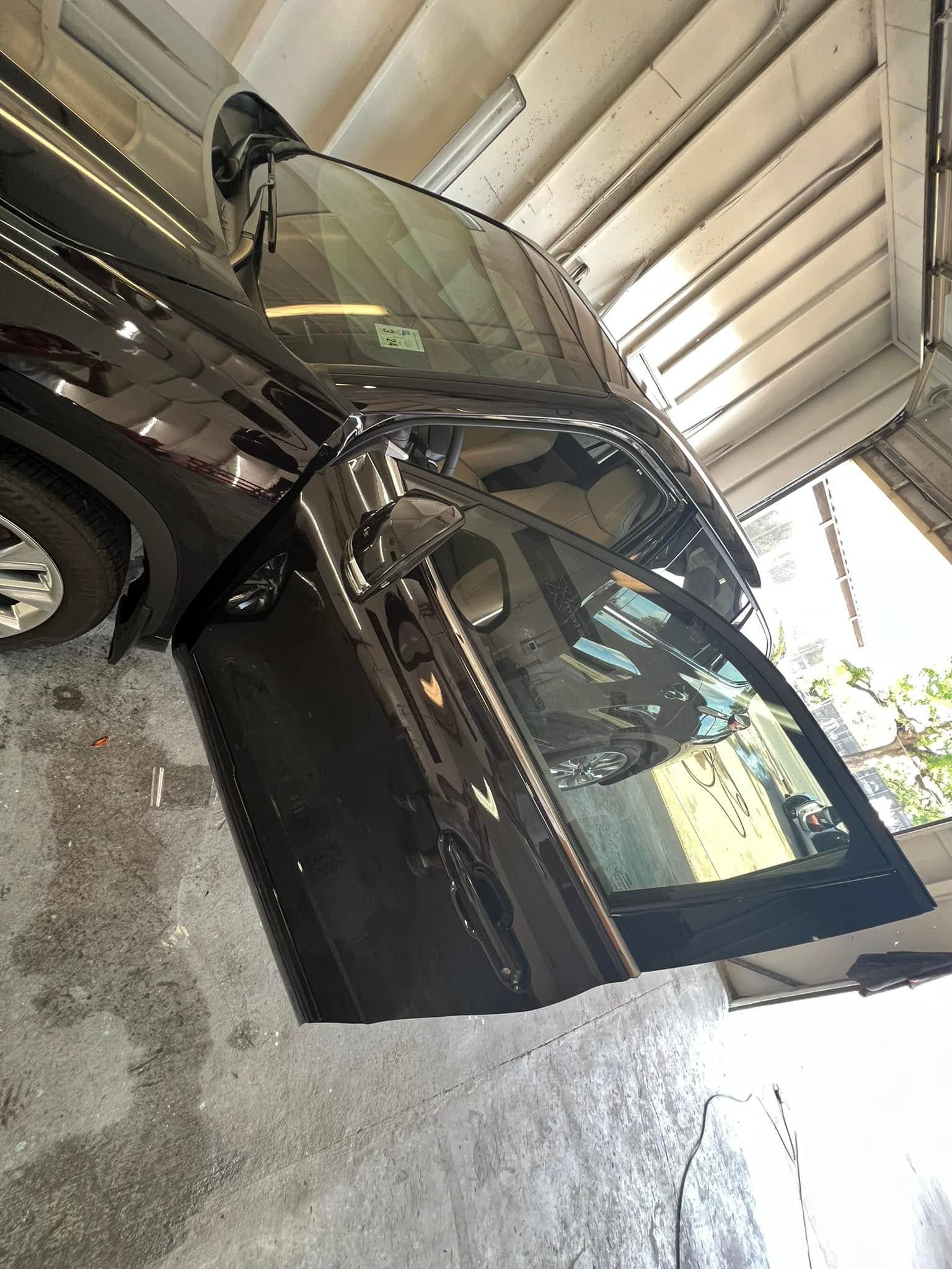 Black car parked in a covered carport, driver door open, with another vehicle beside it.