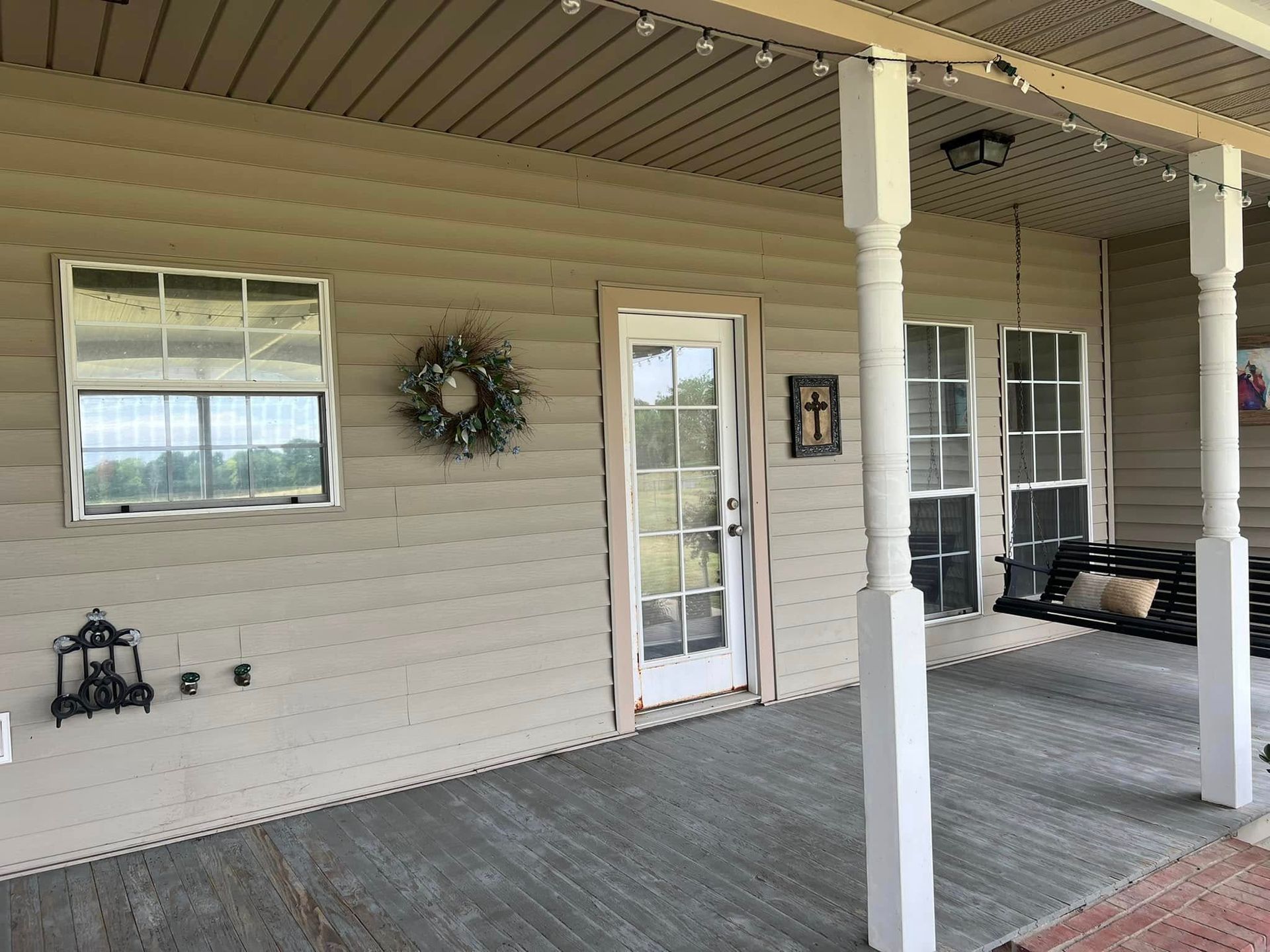 Covered porch with gray siding, white columns, glass door, windows, and a bench.