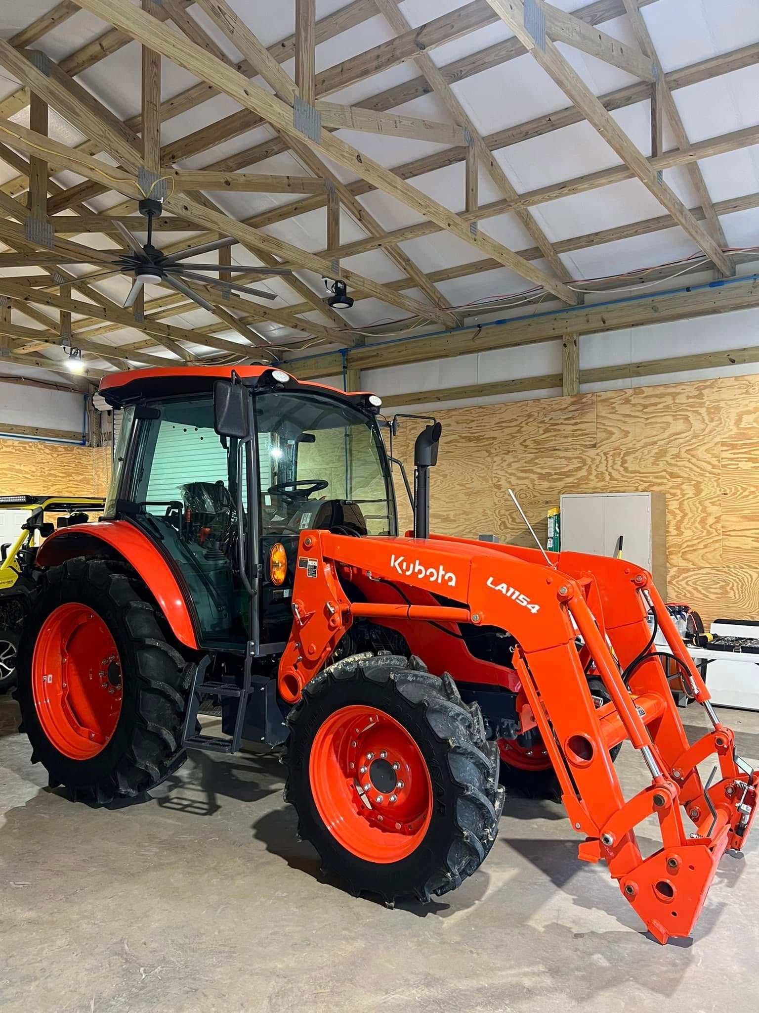 Orange tractor with front loader parked inside a wooden barn or shed