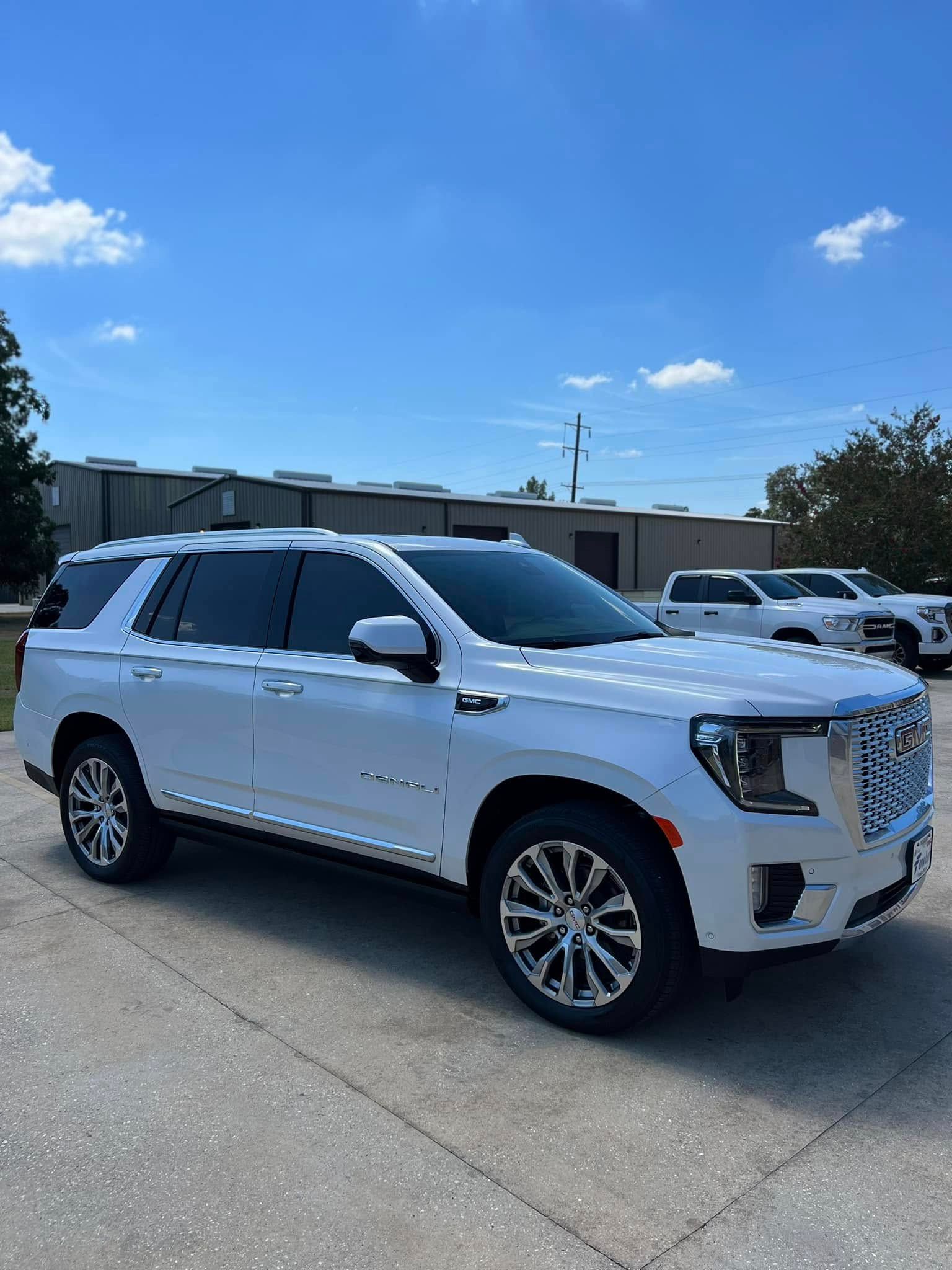 White GMC SUV parked on a sunny lot with low buildings and blue sky in the background