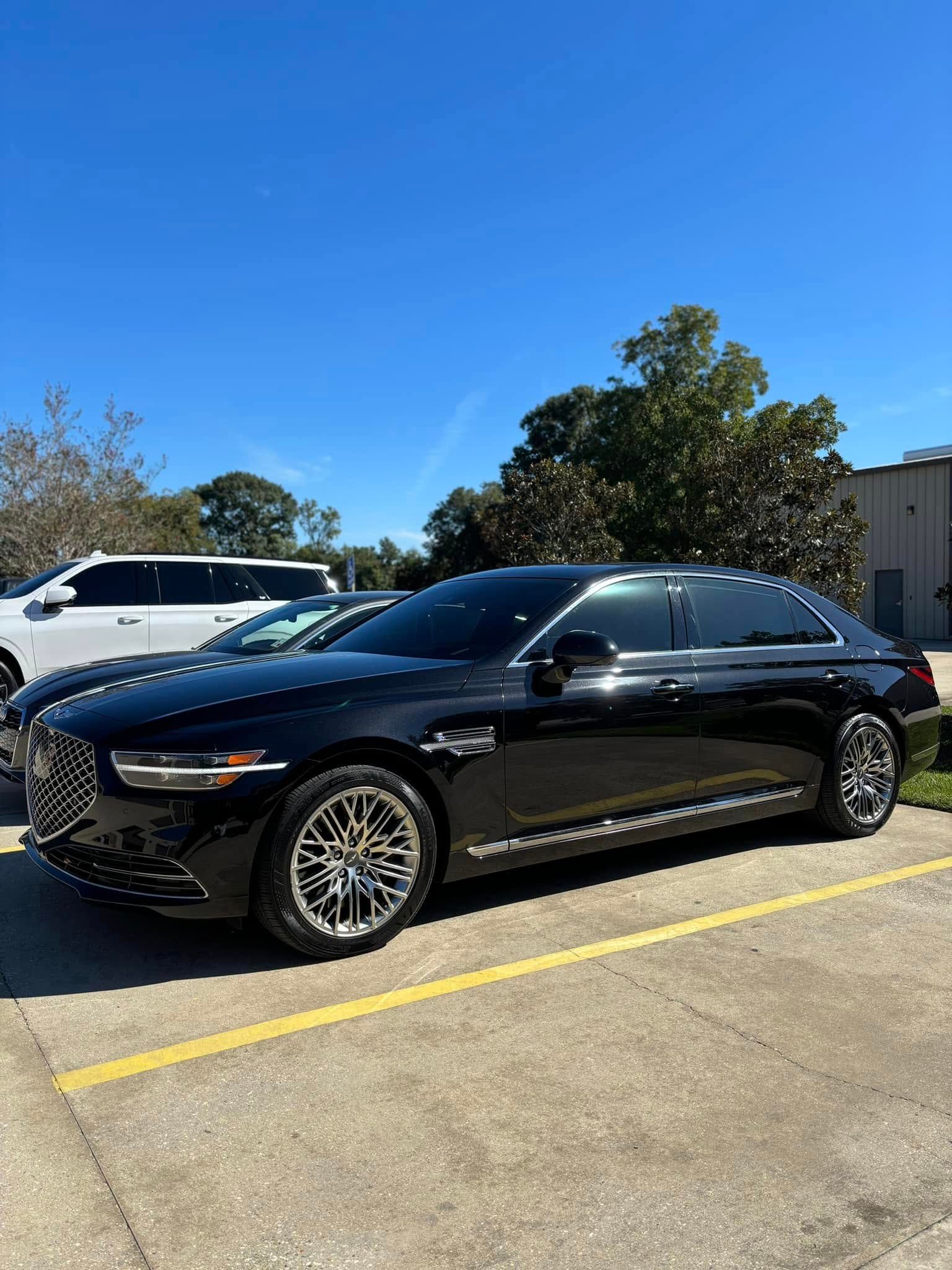 Black sedan parked in a lot on a sunny day, with a white SUV and building in the background.