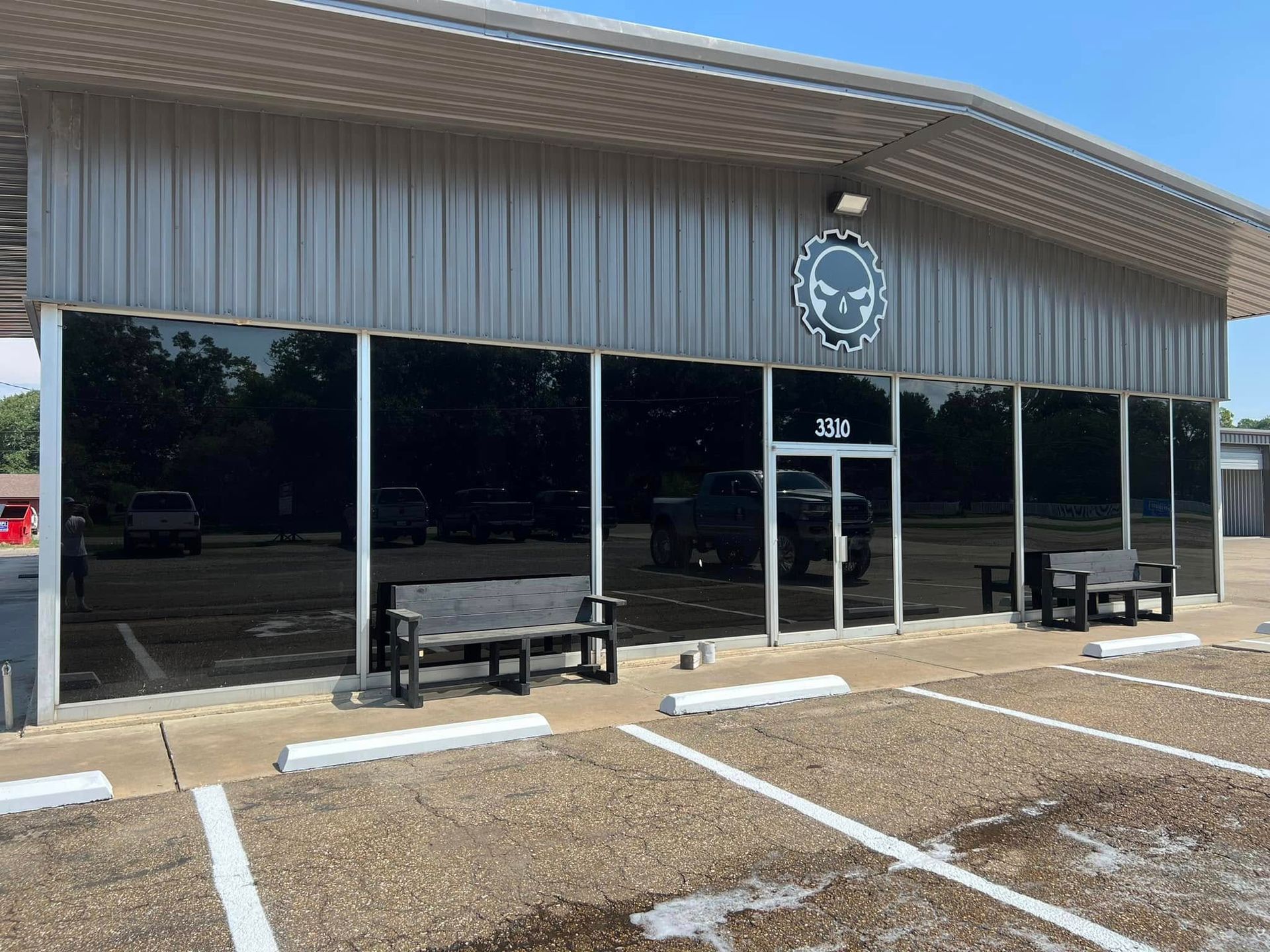 Storefront with dark windows, metal awning, bench, and parking spaces in front
