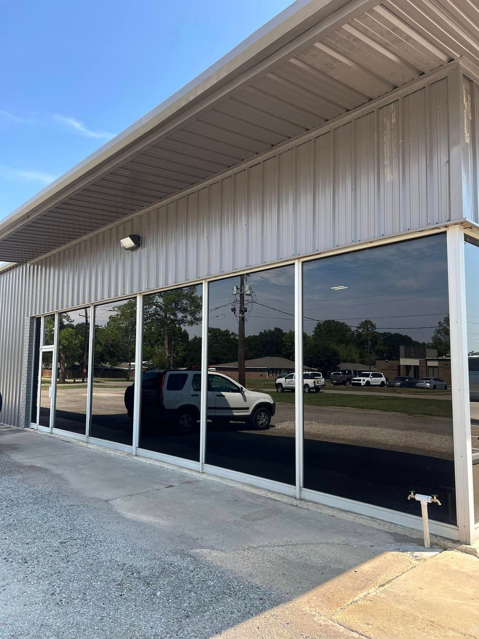 Storefront with large reflective windows, metal awning, and gravel parking lot under a blue sky