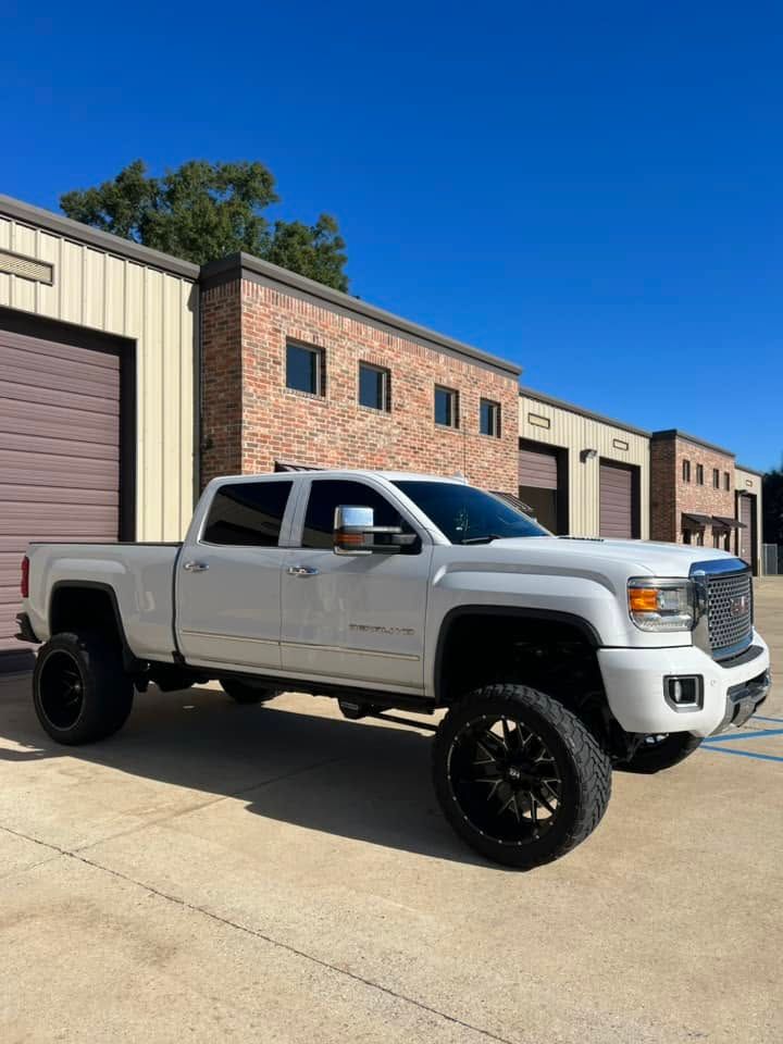 White lifted pickup truck parked outside brick commercial buildings under a clear blue sky