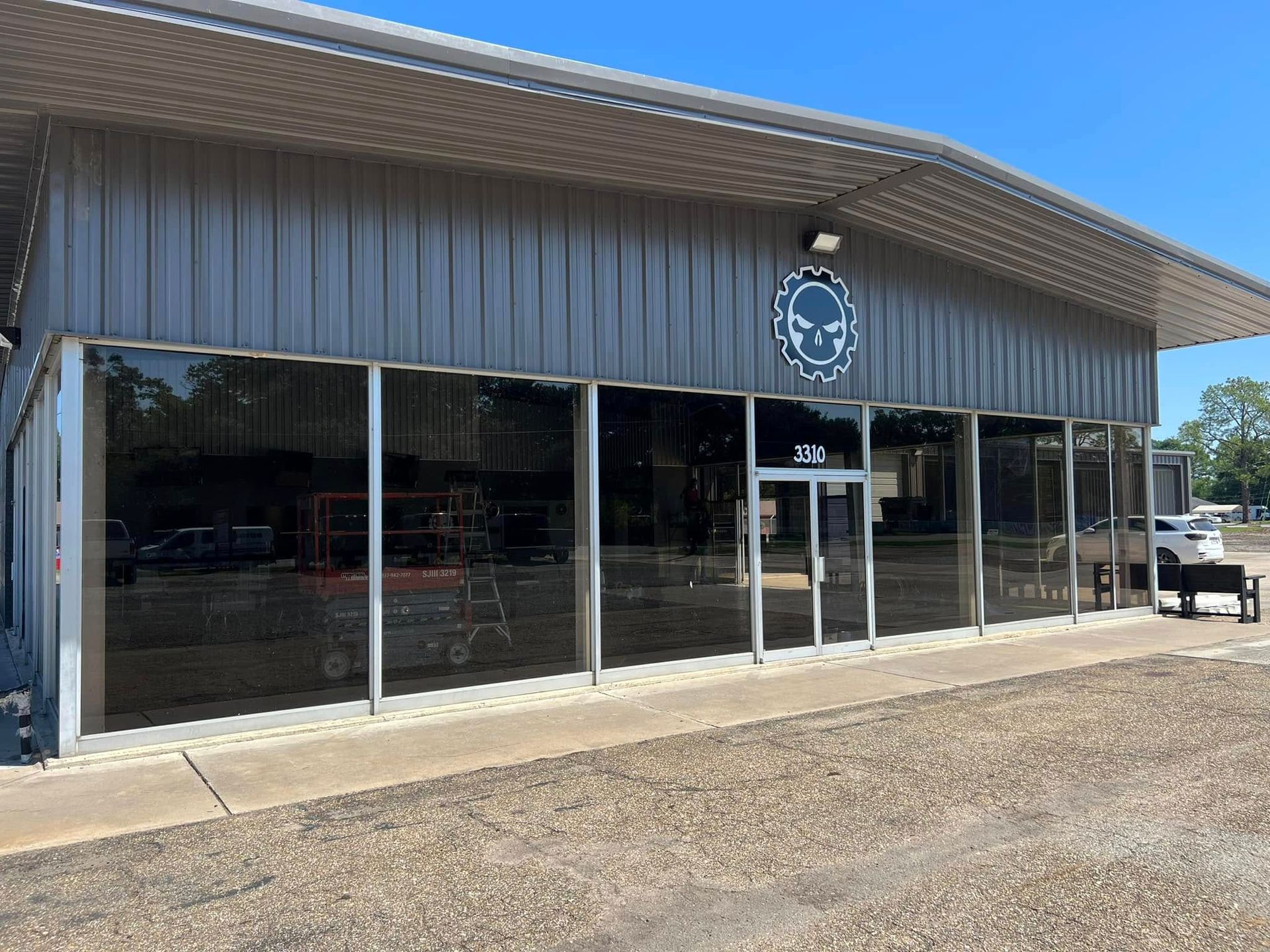 Storefront with large glass windows, metal siding, and a sign under a clear blue sky