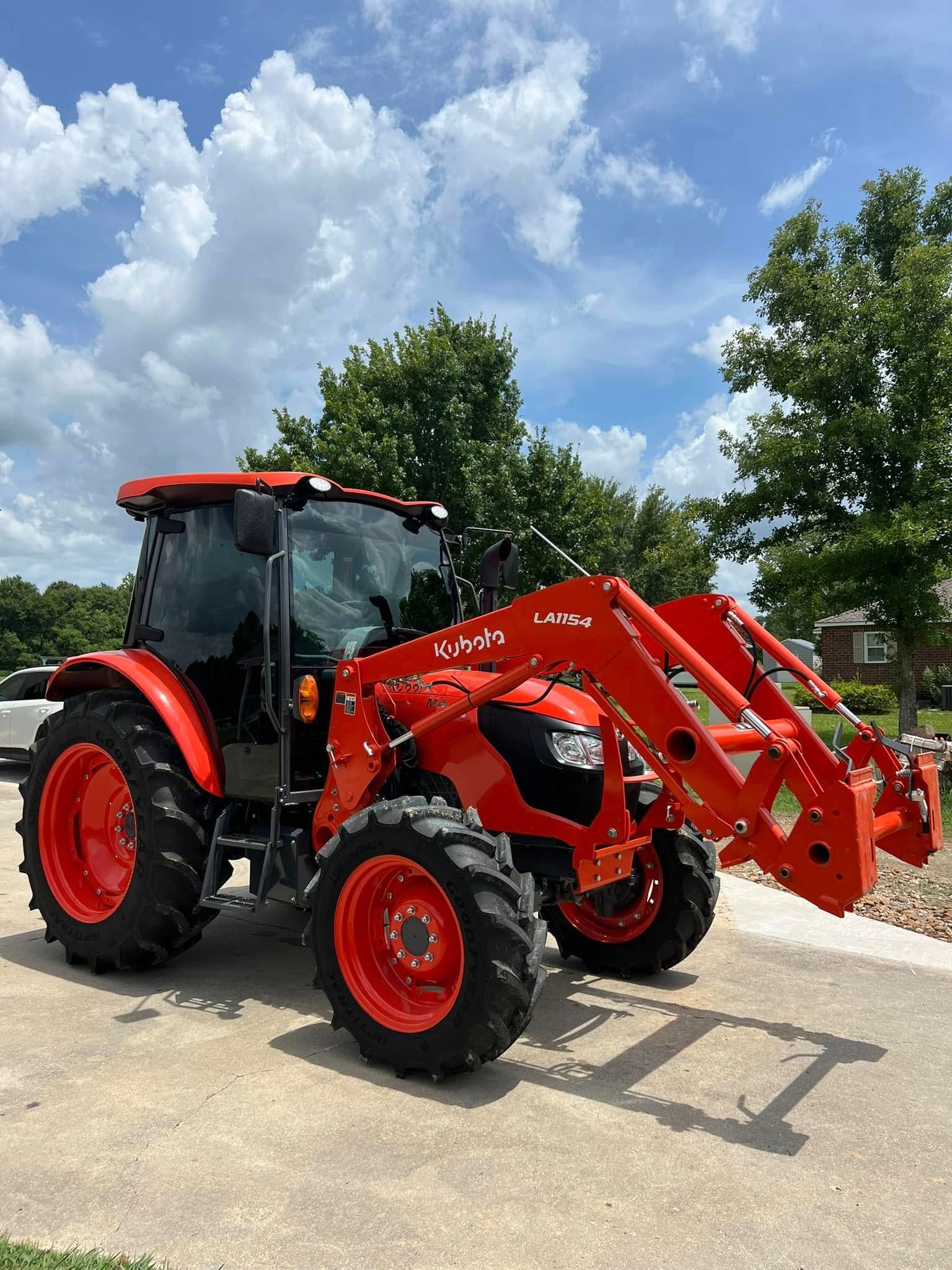 Red tractor with front loader parked outdoors under a blue sky and trees.