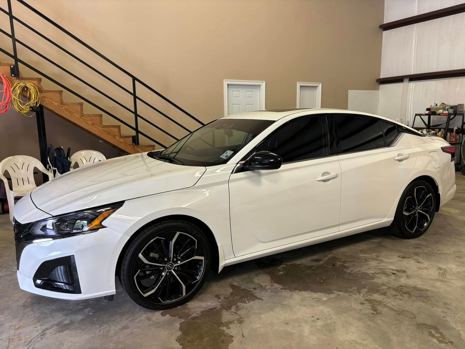 White sedan with black wheels parked inside a garage near stairs