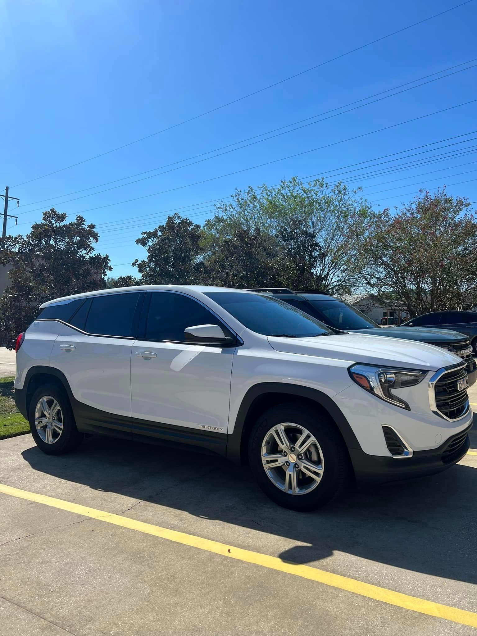 White SUV parked in a lot under a clear blue sky, viewed from the side.