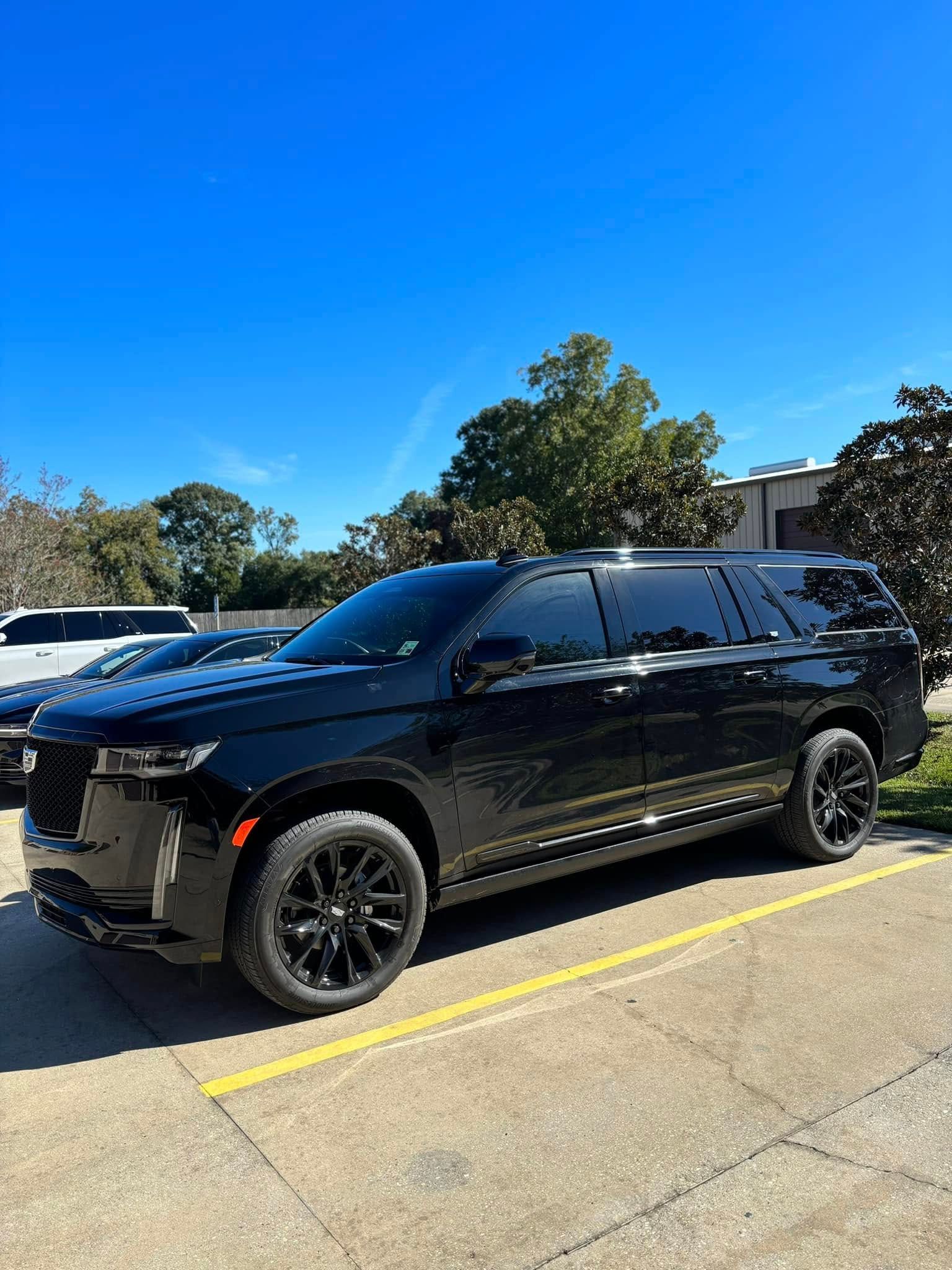 Black SUV parked in a sunny lot with yellow lines and trees in the background