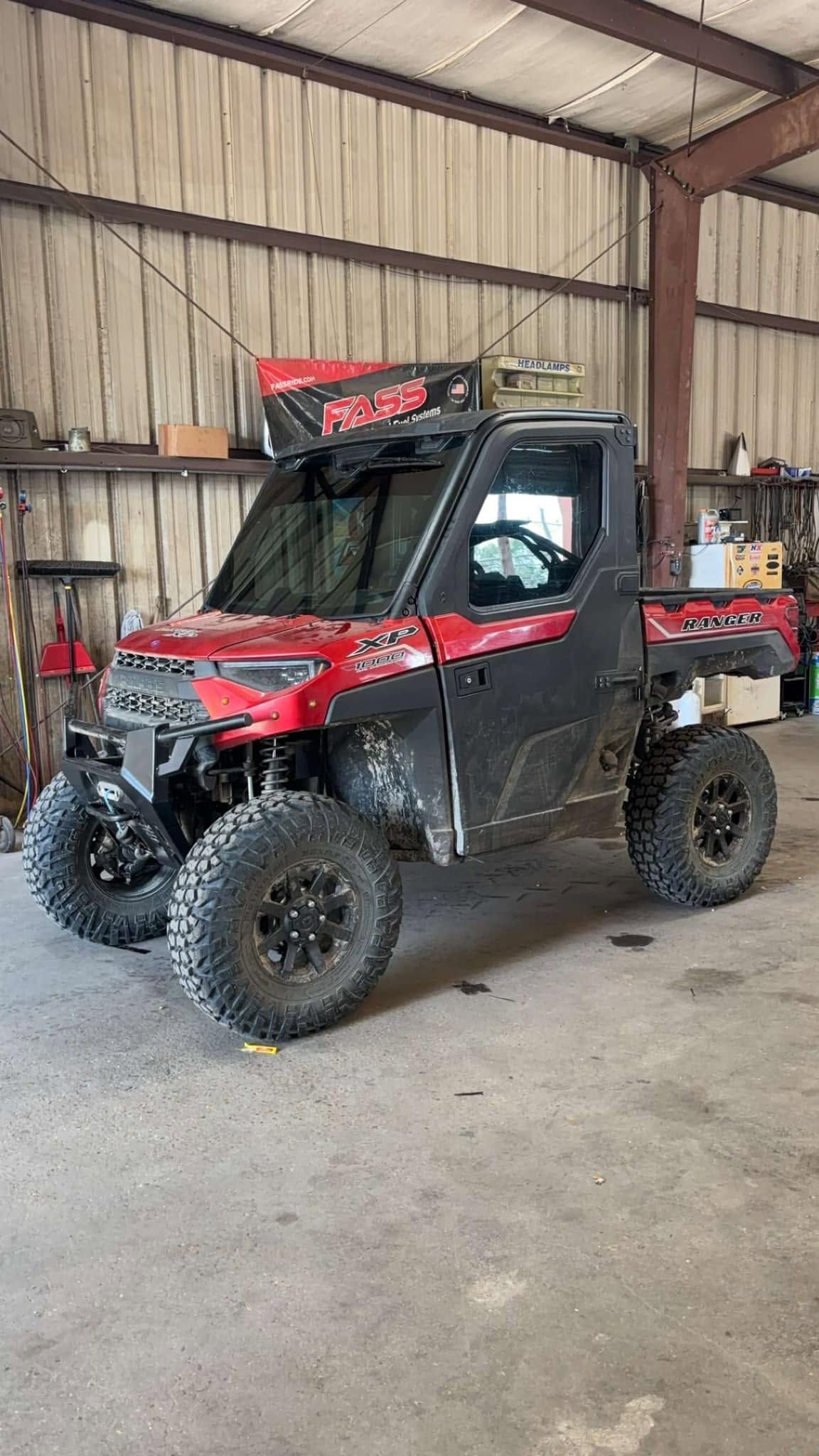 Red and black off-road utility vehicle parked inside a metal workshop or barn.