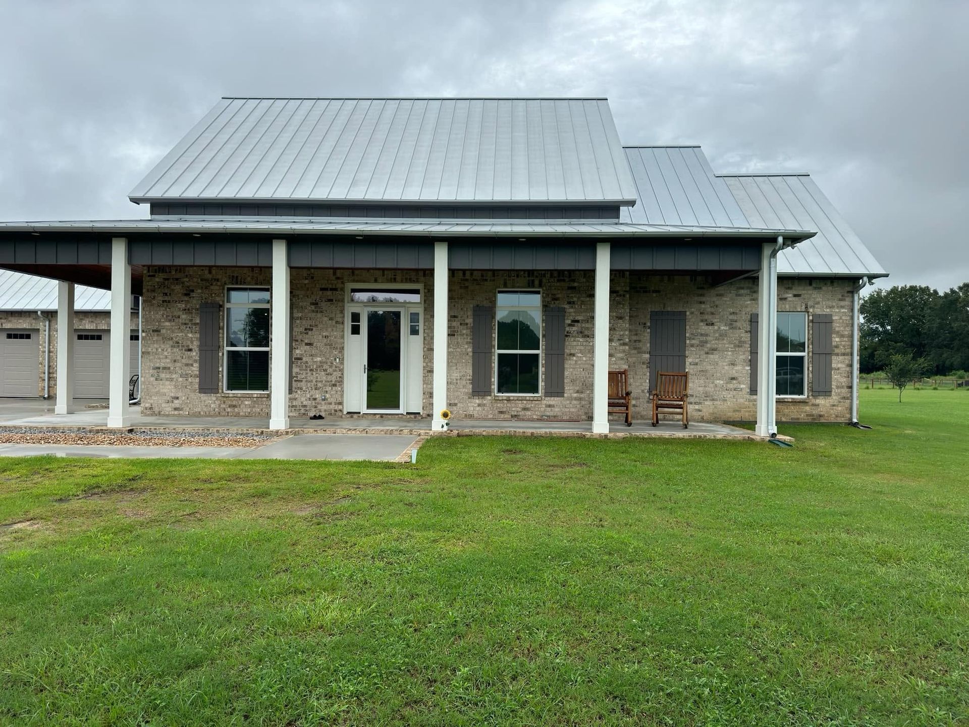 Stone house with metal roof and covered porch in a grassy yard under cloudy skies