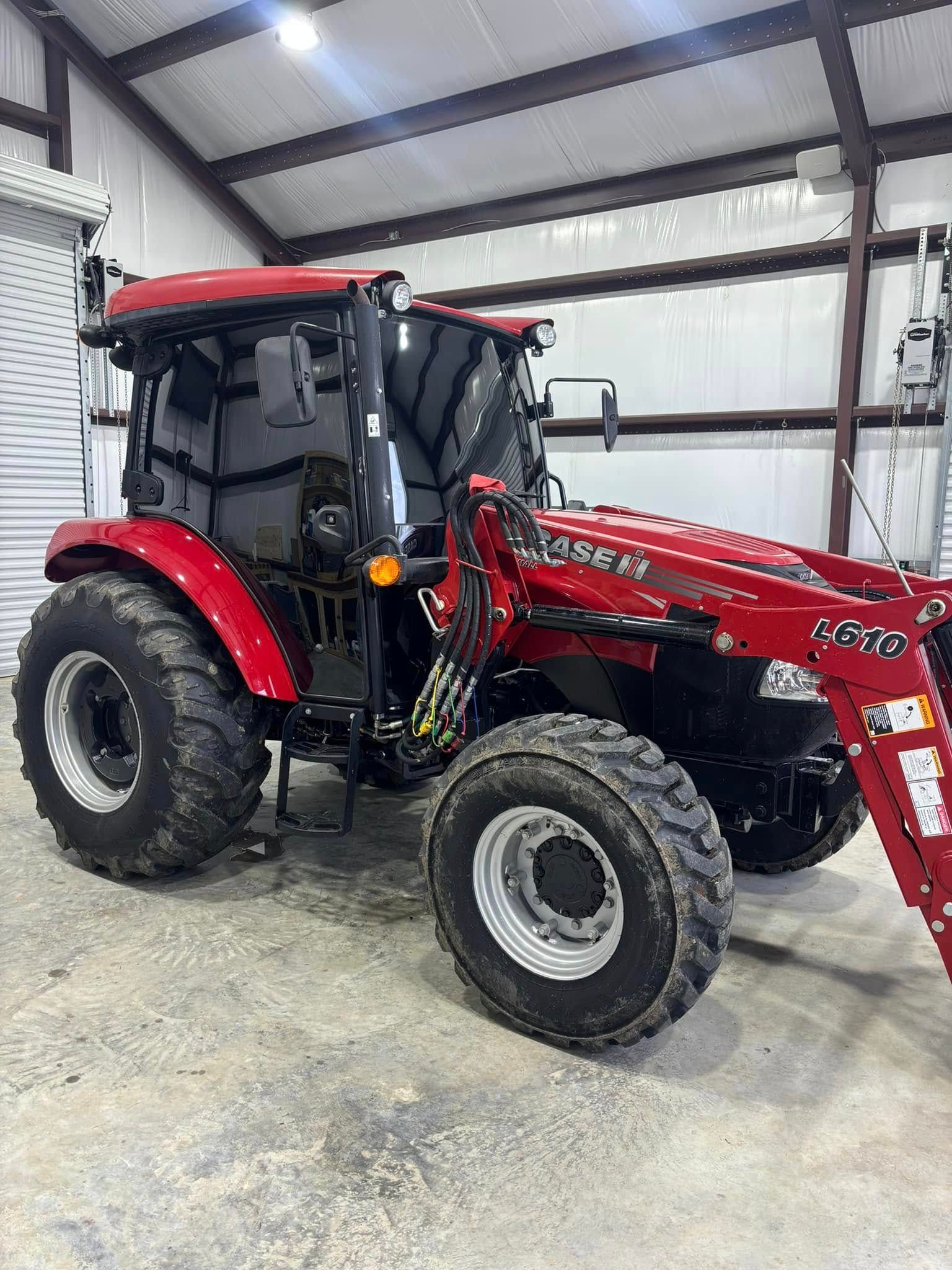 Red tractor with front loader parked inside a metal barn