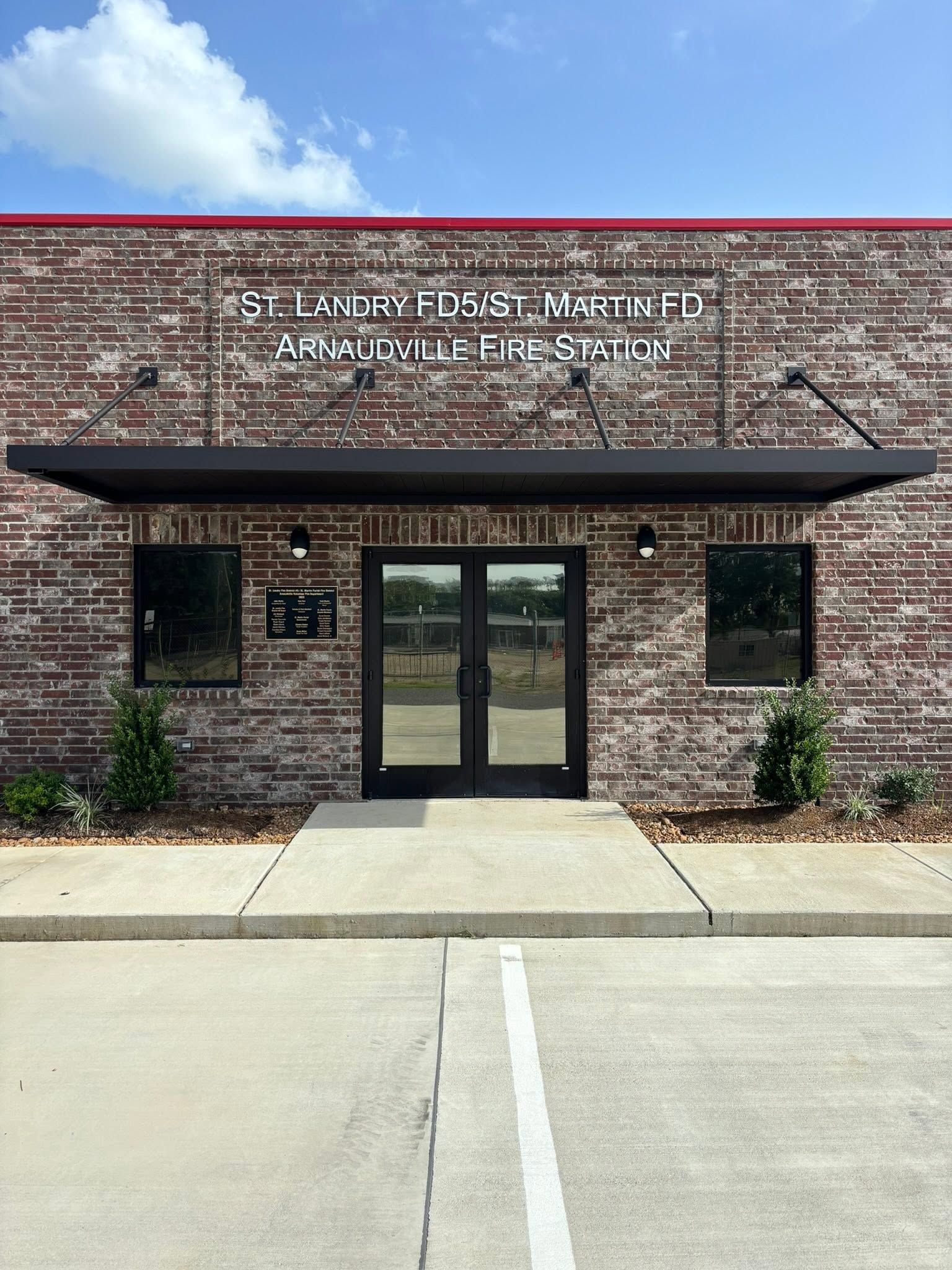Brick building entrance with double glass doors, black awning, and white lettering under a blue sky.