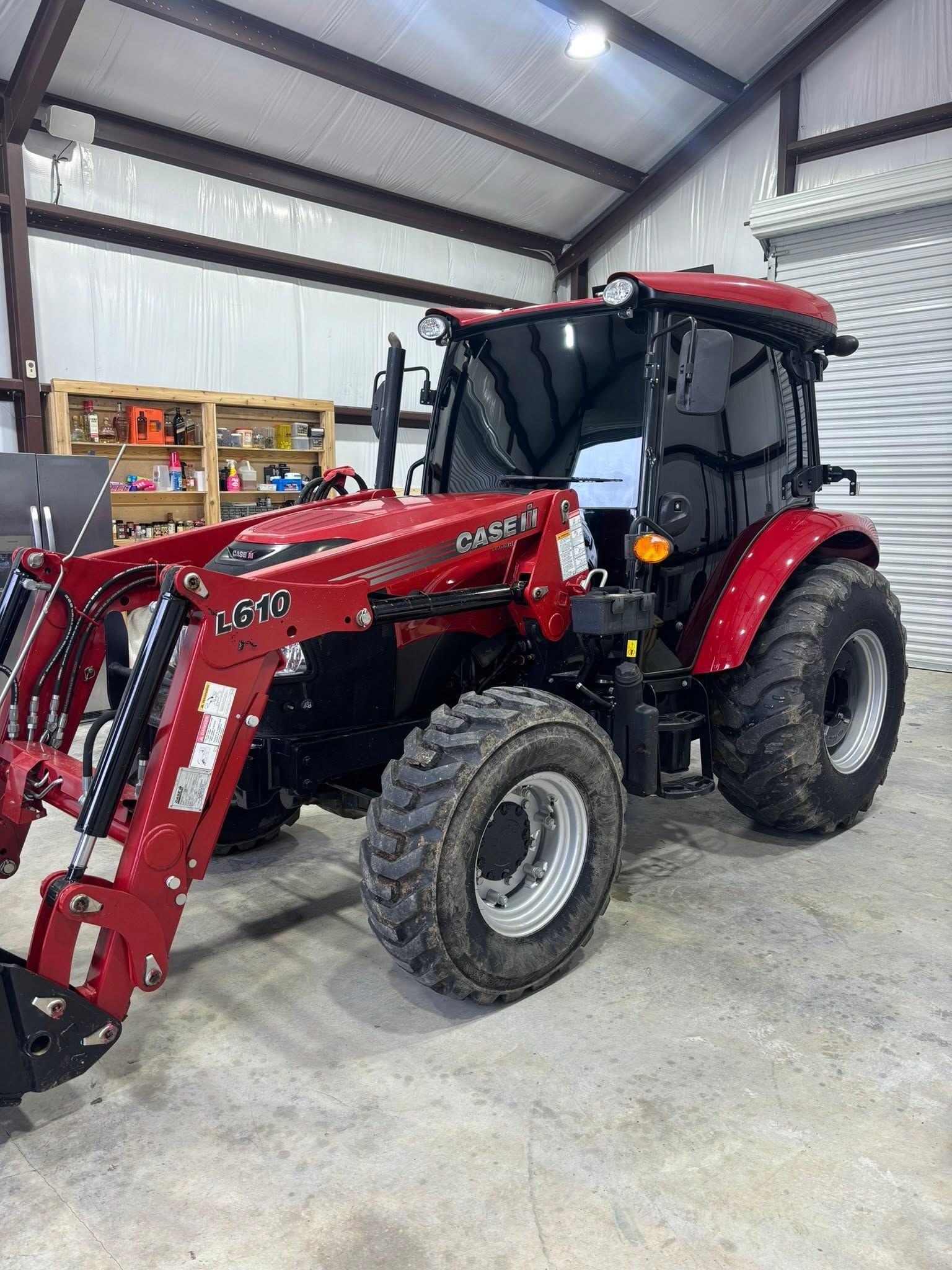 Red tractor with front loader parked inside a metal workshop.