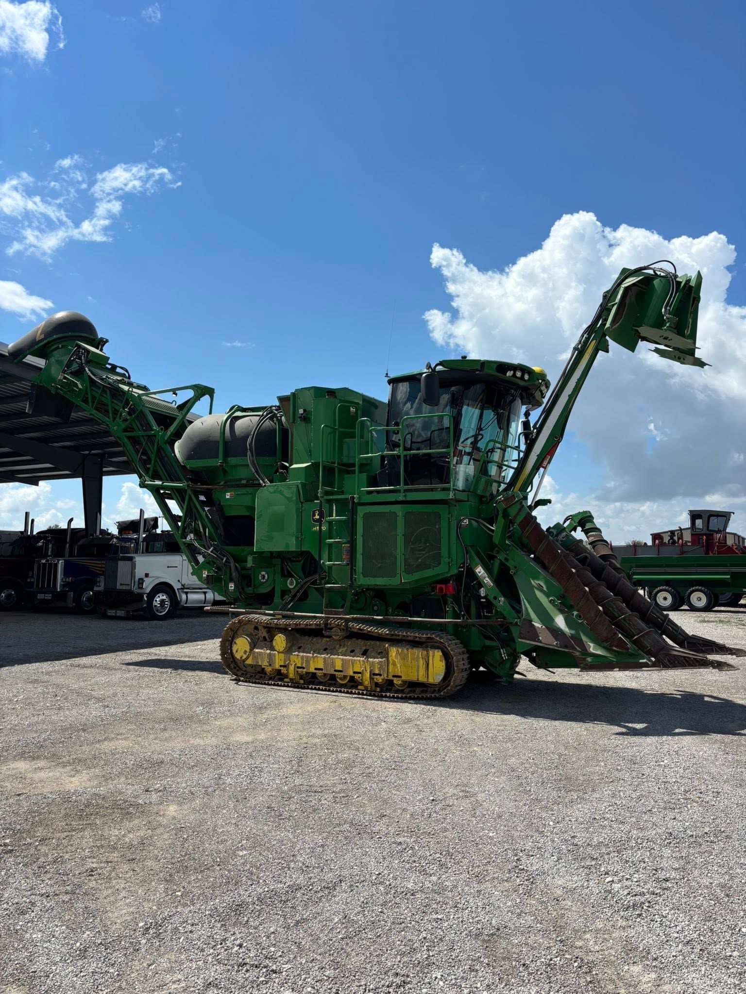 Green tracked industrial machine on a gravel lot under a bright blue sky