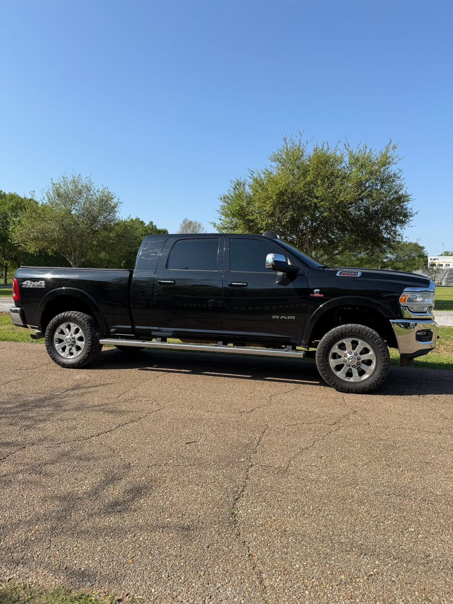 Black pickup truck parked on gravel under a clear blue sky with trees behind it