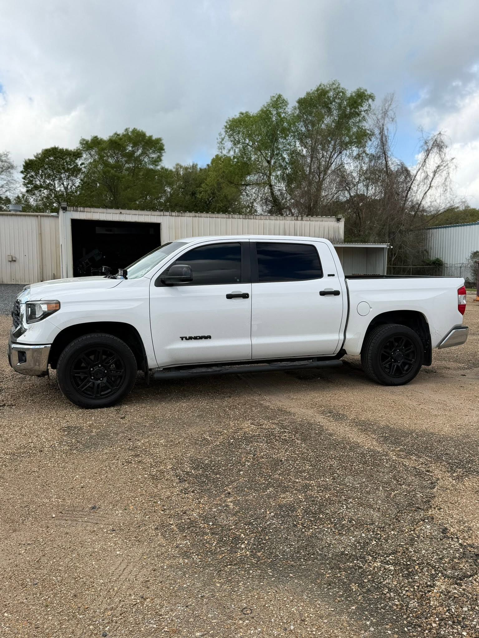 White lifted pickup truck parked on gravel beside a shed, with tinted windows and black wheels