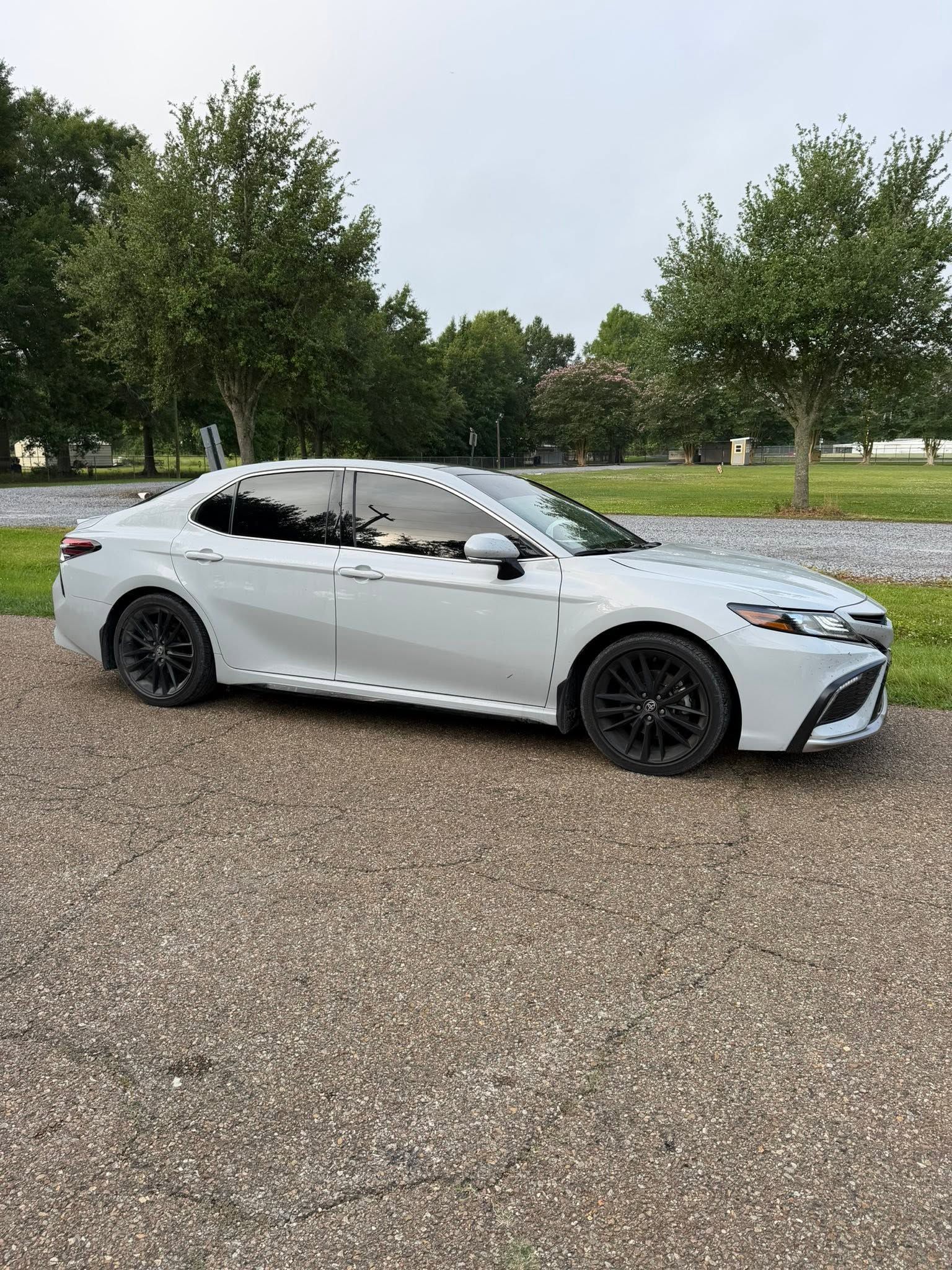 White sedan parked on a gravel lot with trees and grass in the background