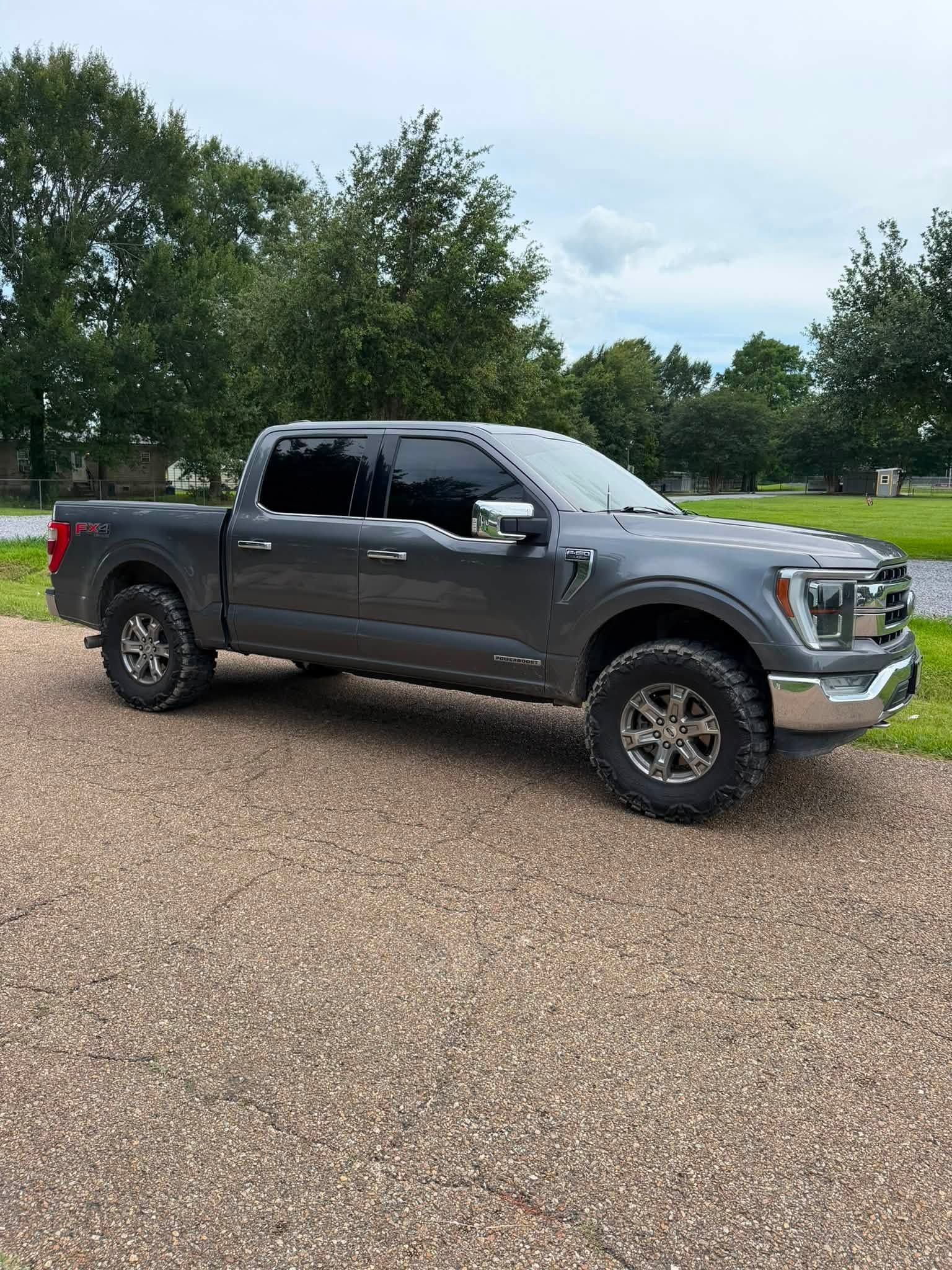 Gray pickup truck parked on a gravel lot with trees in the background.