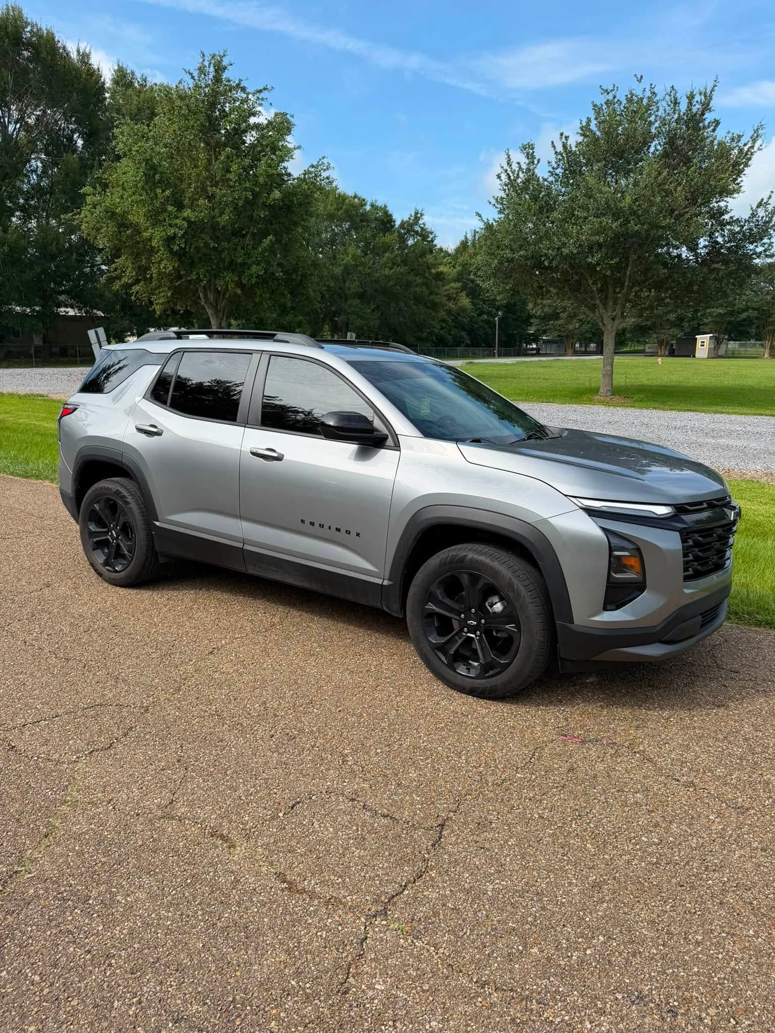 Silver SUV parked on a gravel drive beside a grassy park under a blue sky