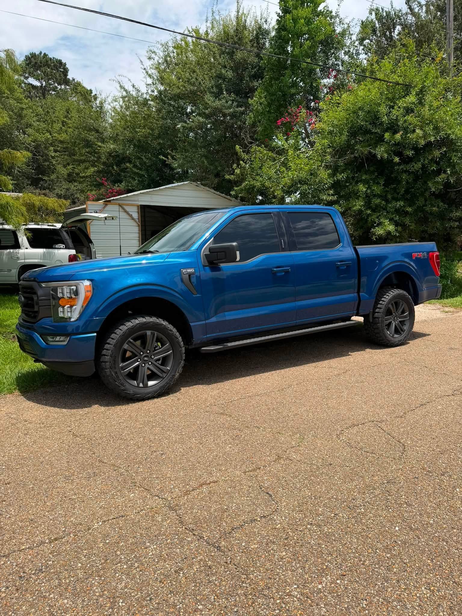 Blue pickup truck parked on a gravel driveway beside a house and trees