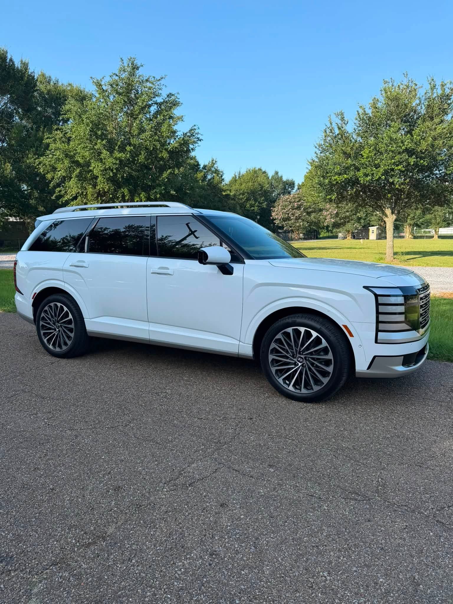 White SUV parked on gravel near trees under a clear blue sky