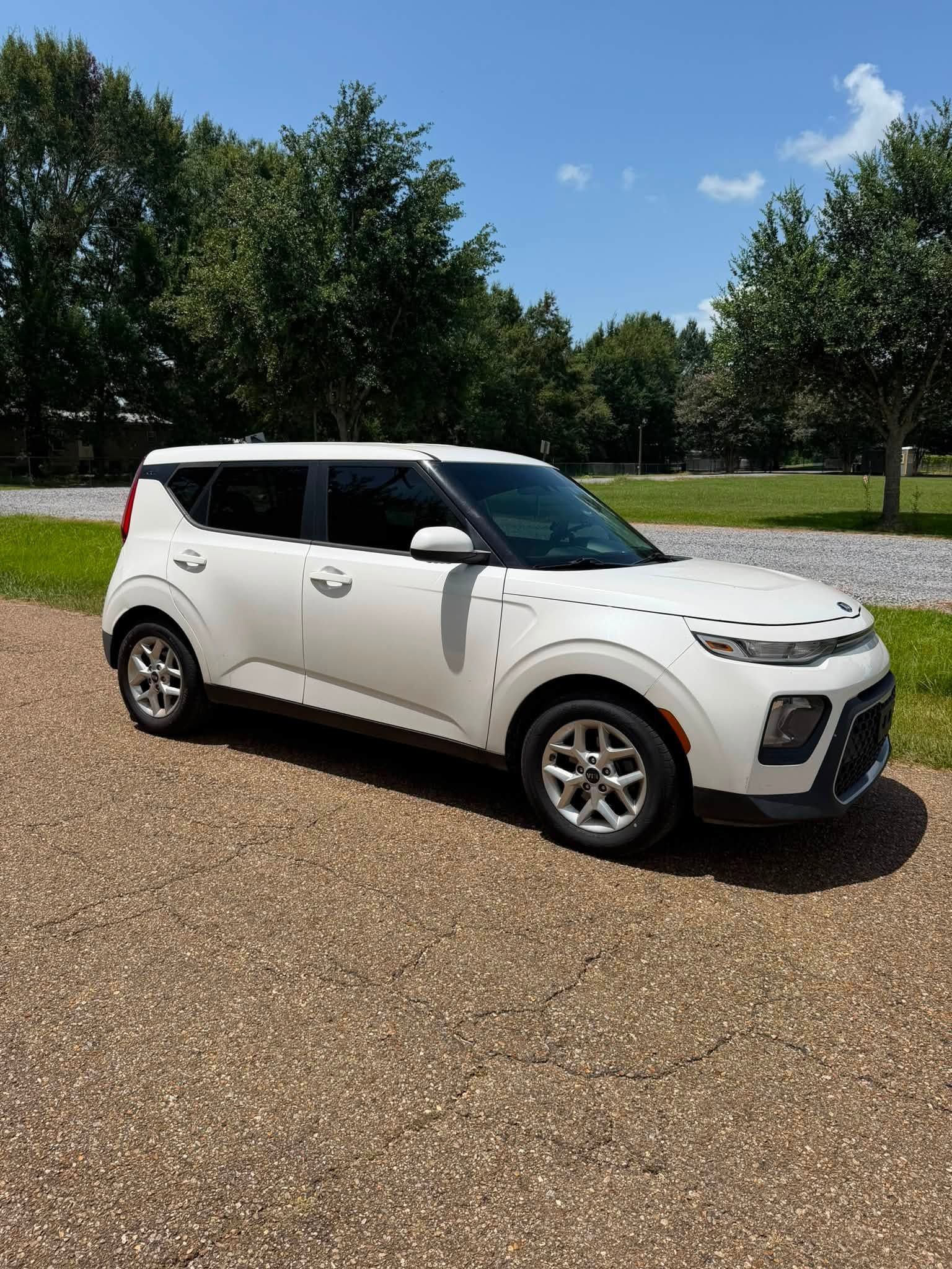 White compact SUV parked on a gravel lot with trees and blue sky in the background