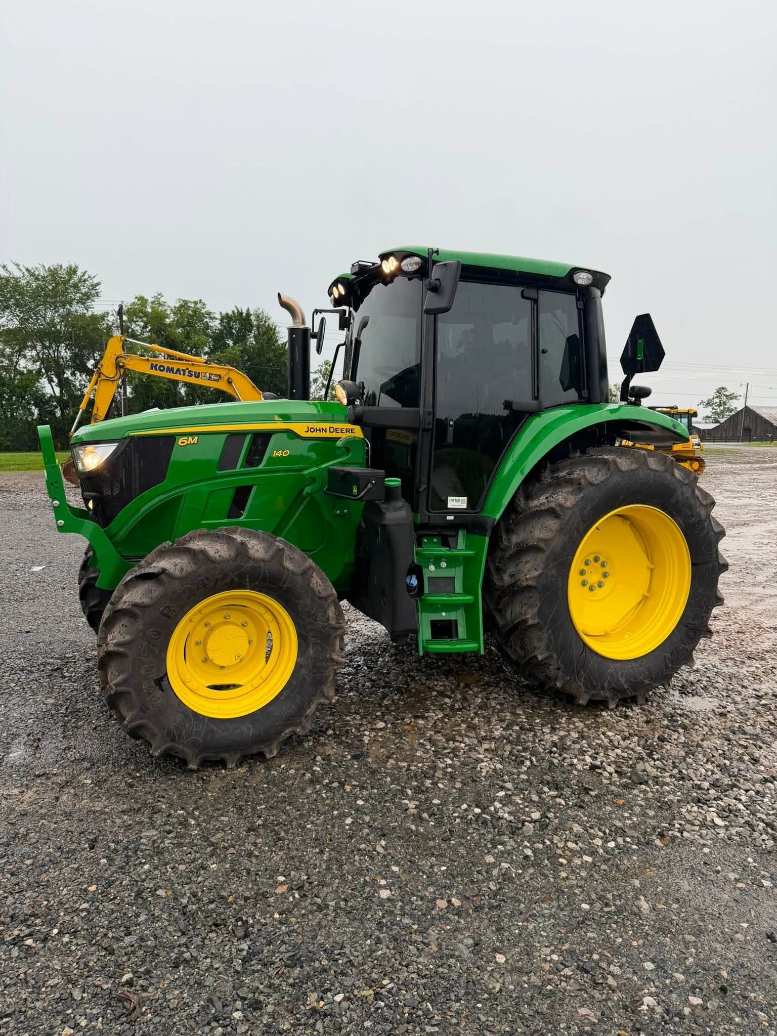 Green tractor with yellow wheels parked on a gravel lot under an overcast sky