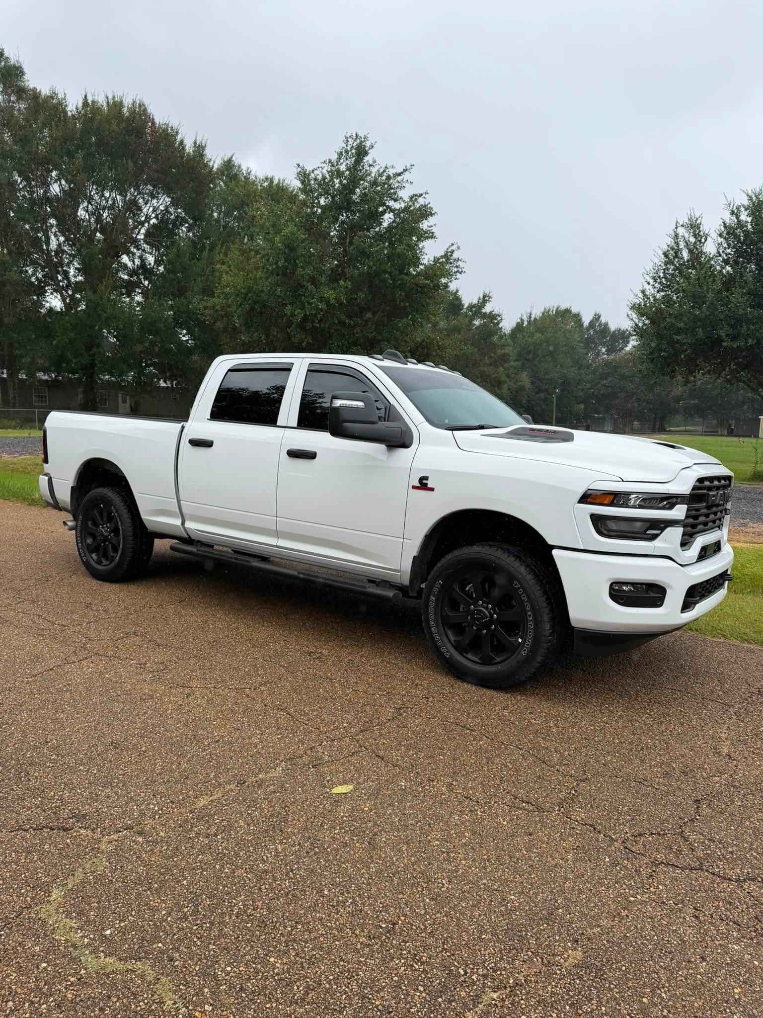 White pickup truck with black wheels parked on a gravel lot near trees