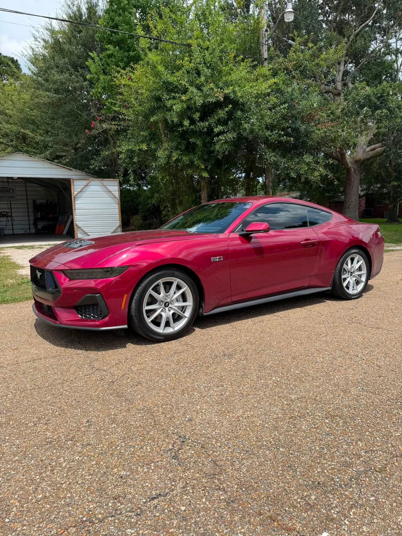 Red sports coupe parked on a gravel driveway beside a house and trees
