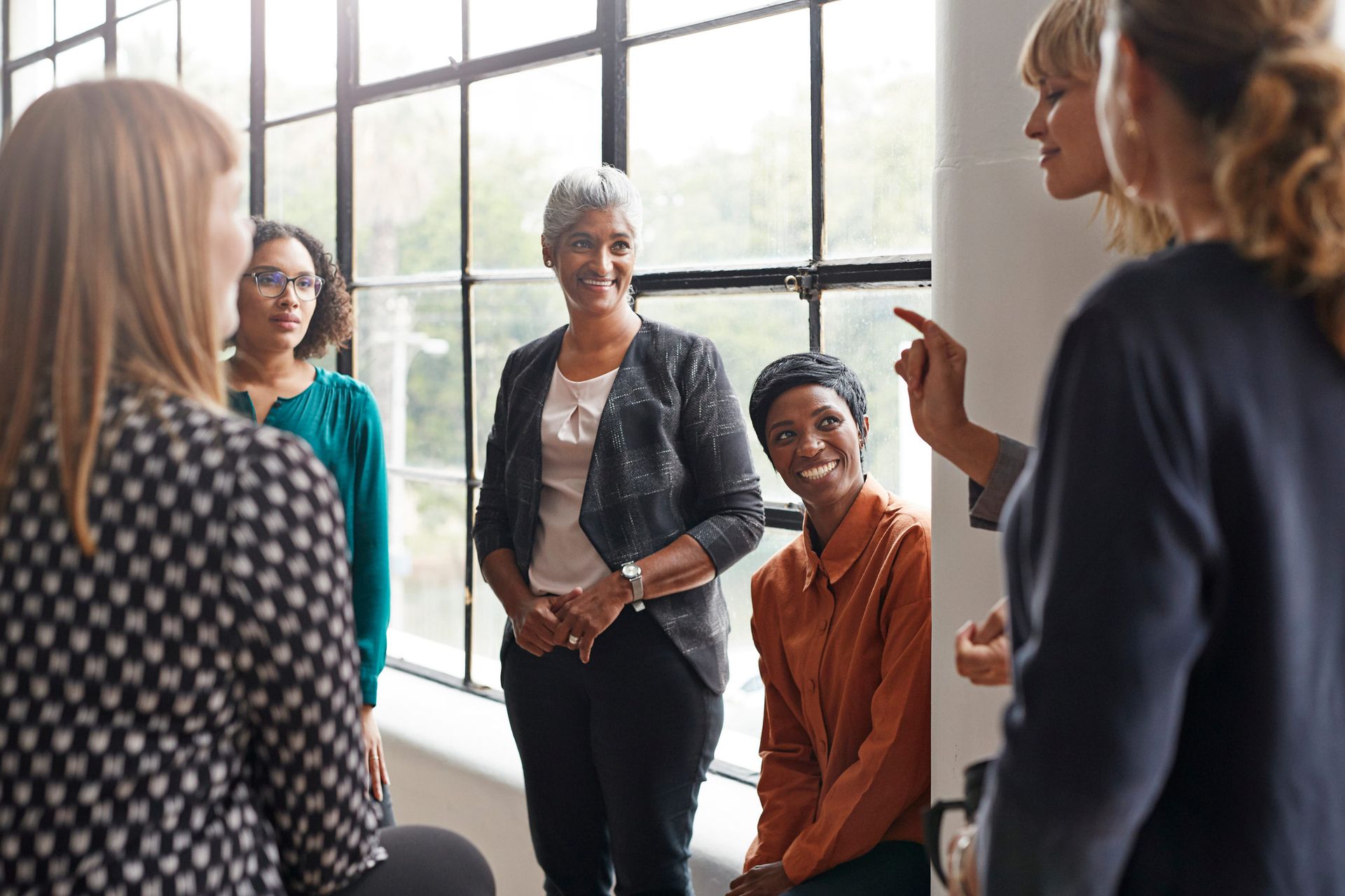 Group of people in discussion near a window, smiling and gesturing.