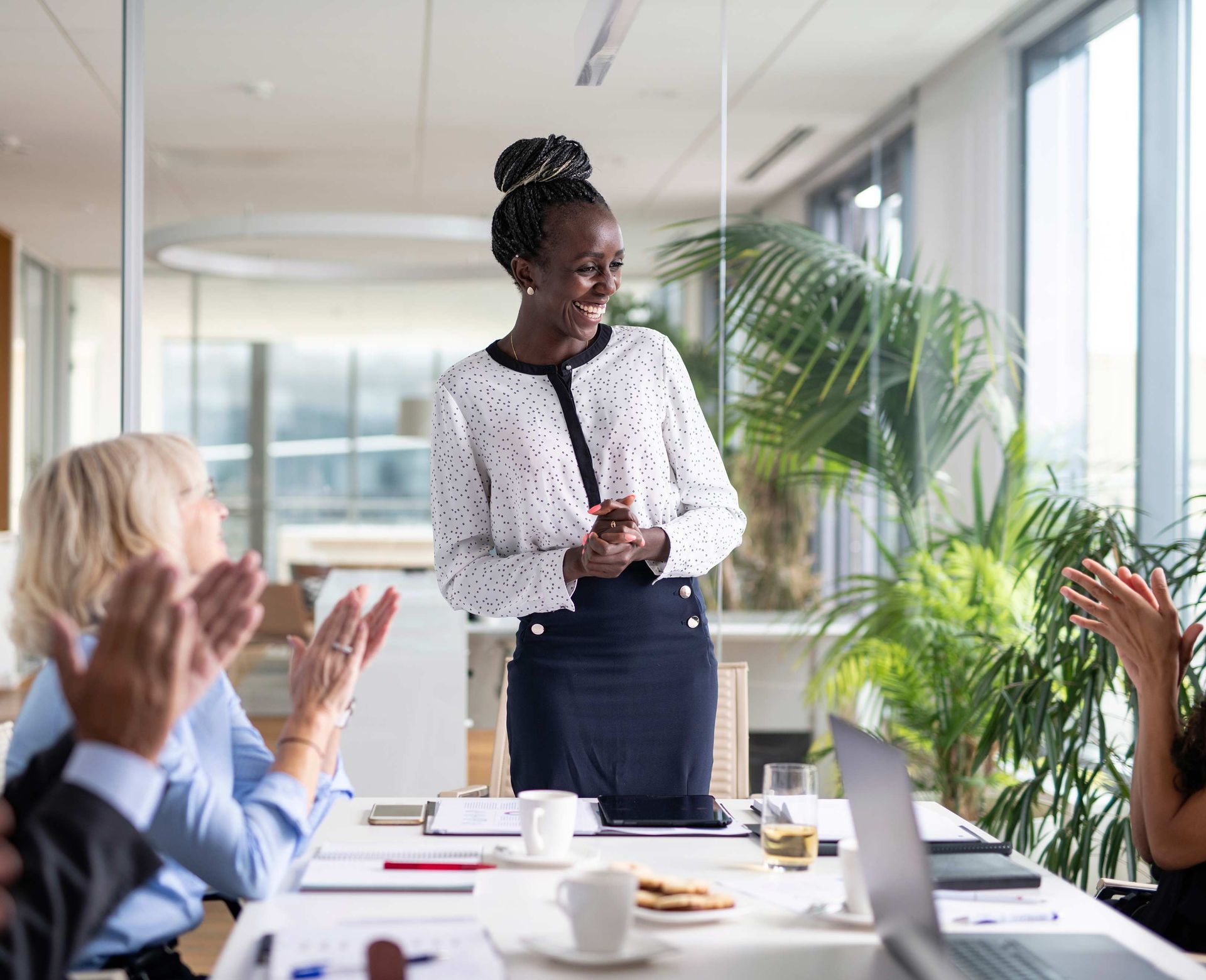 Woman smiles while receiving applause in a bright office meeting room.