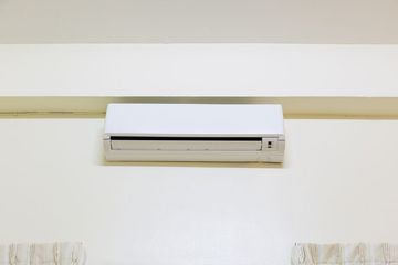 A white mini-split air conditioning unit mounted on a plain, light-colored wall.