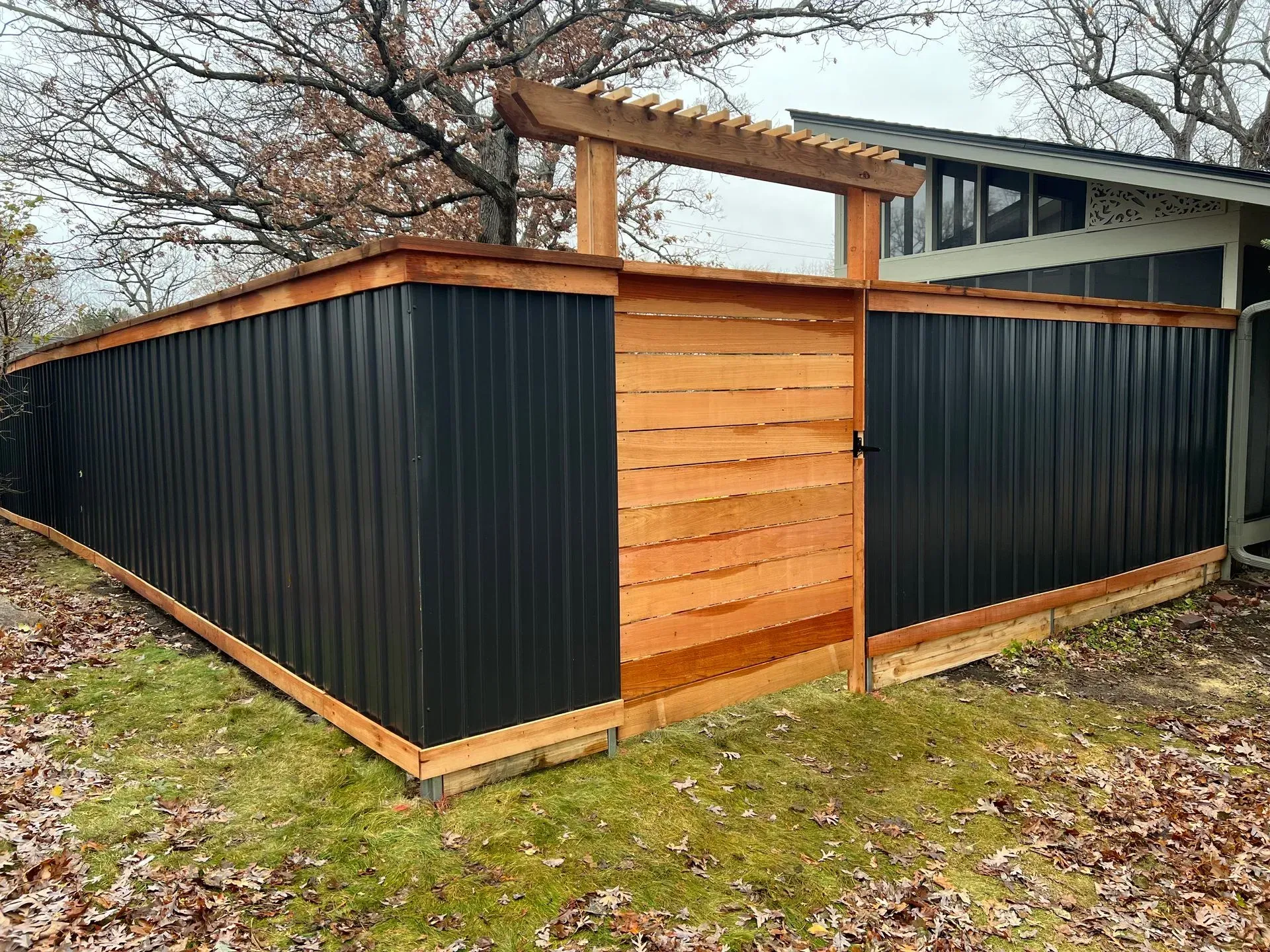 A black fence with a wooden gate in front of a house.