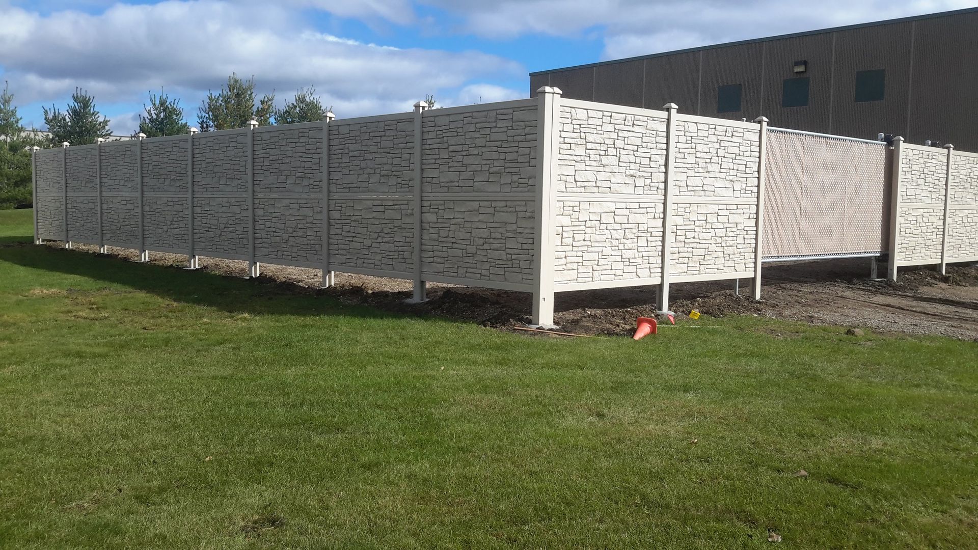 White privacy fence around a grassy yard beside a building under a partly cloudy sky