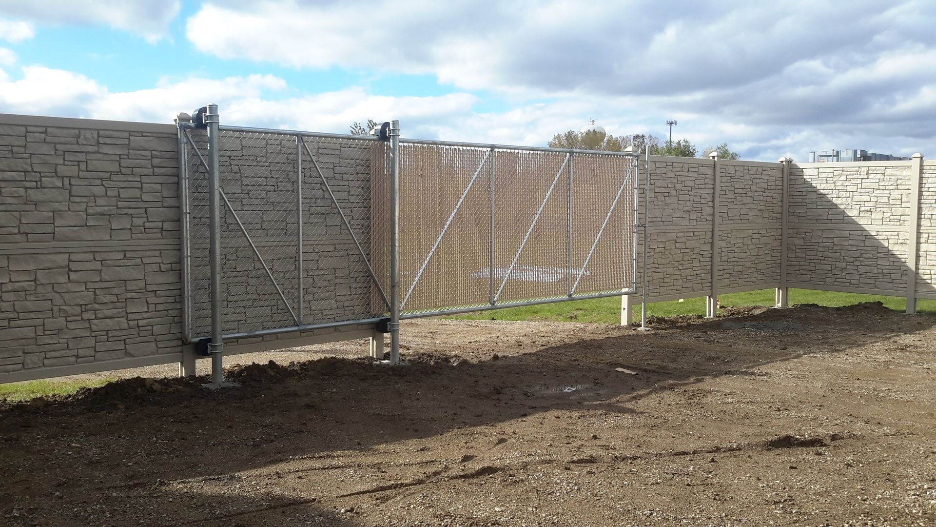 Stone wall and metal gate enclosing a dirt yard under a bright sky.